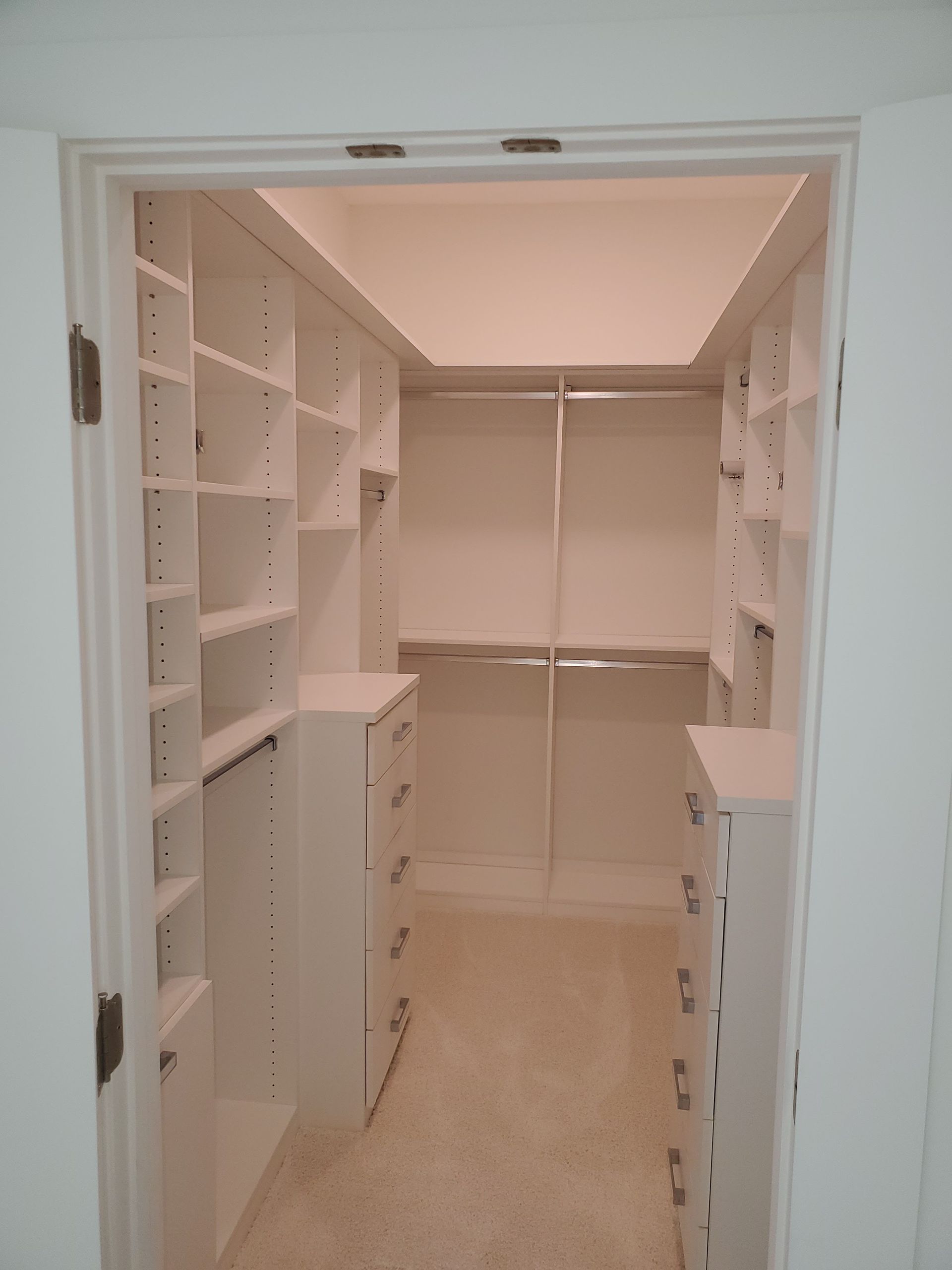 A walk-in closet featuring white shelves, hanging rods, and built-in drawers on both sides with neutral carpeting.