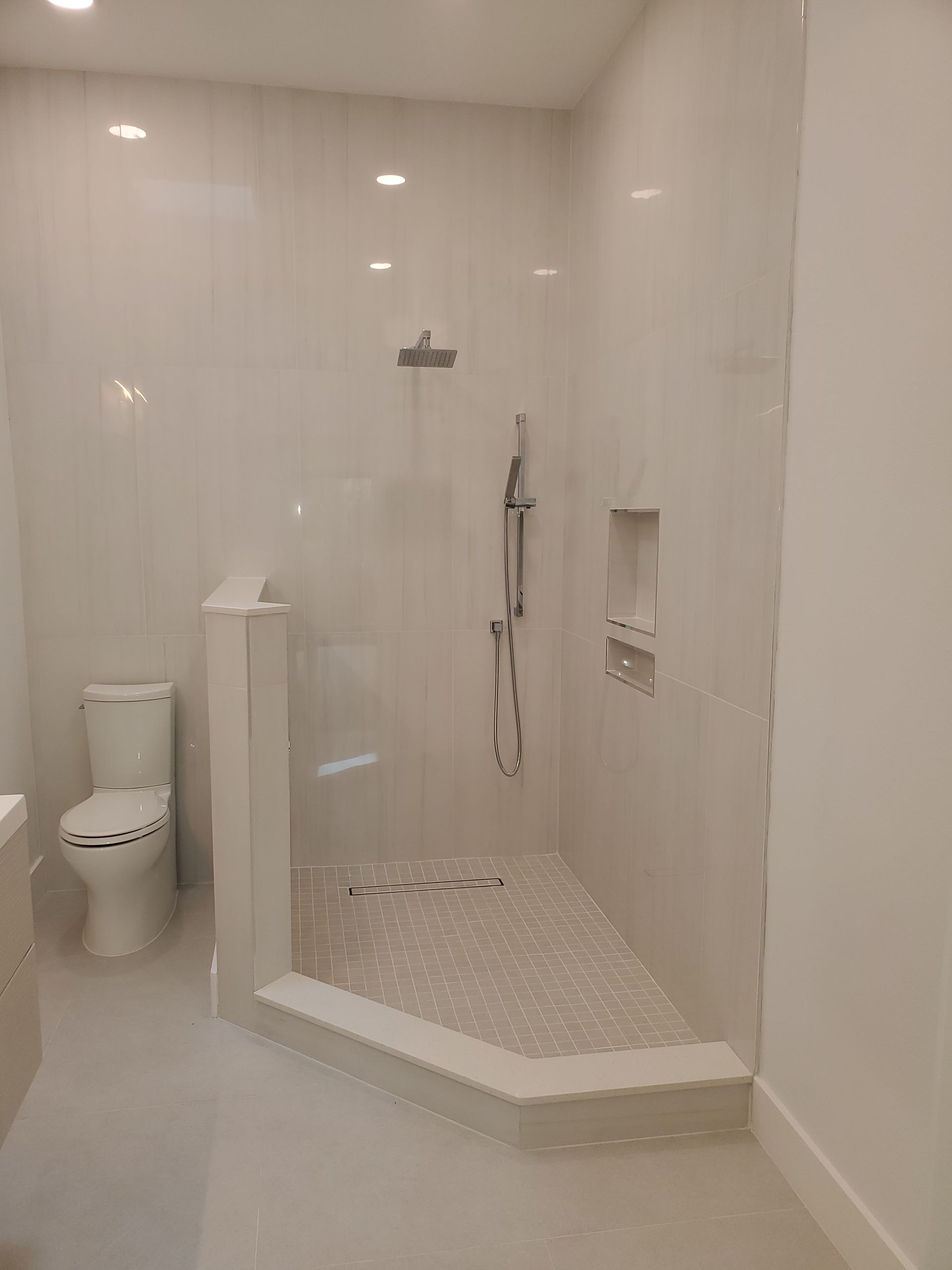 A modern bathroom featuring a white toilet next to a walk-in corner shower with light-colored tile and a built-in niche.