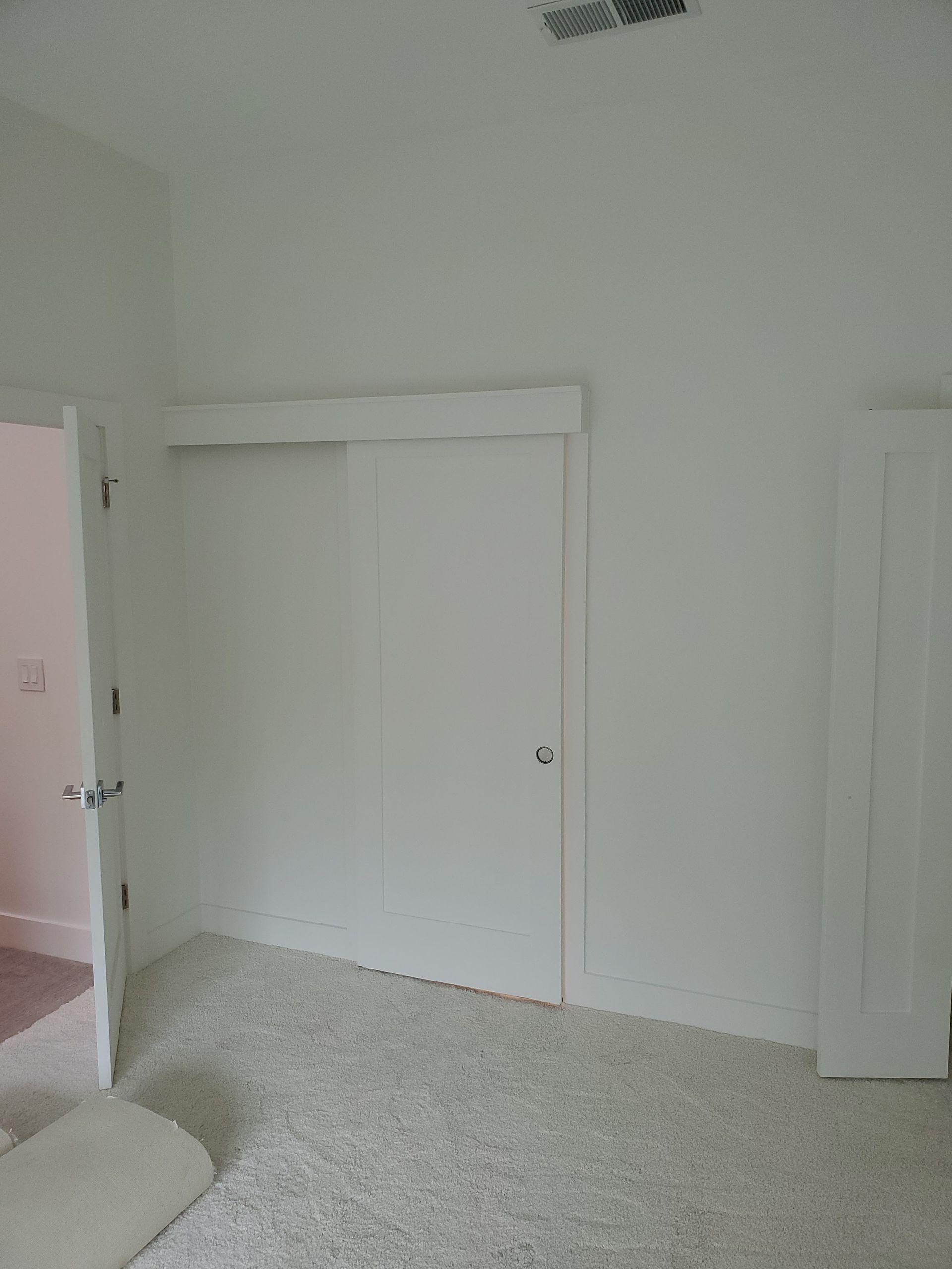 A bedroom interior featuring a closet with white sliding doors and a partially open doorway on the left against white walls.