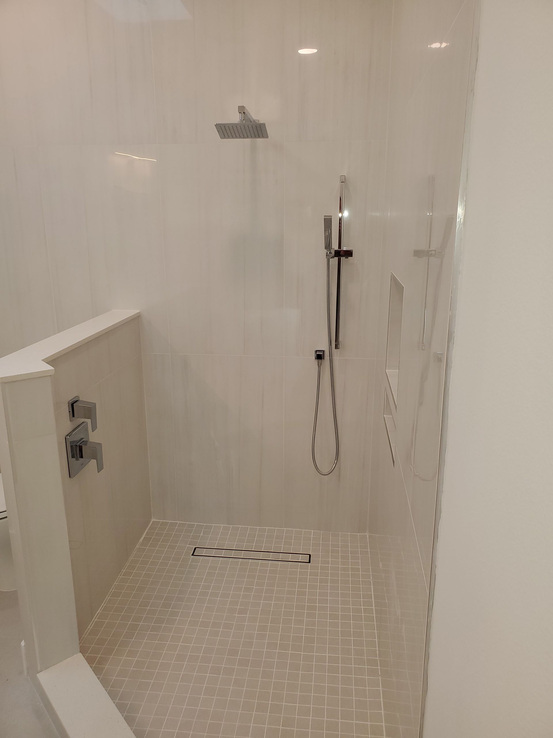 A walk-in shower with white tiled walls, a square overhead rainfall showerhead, a silver handheld sprayer, and mosaic tile.