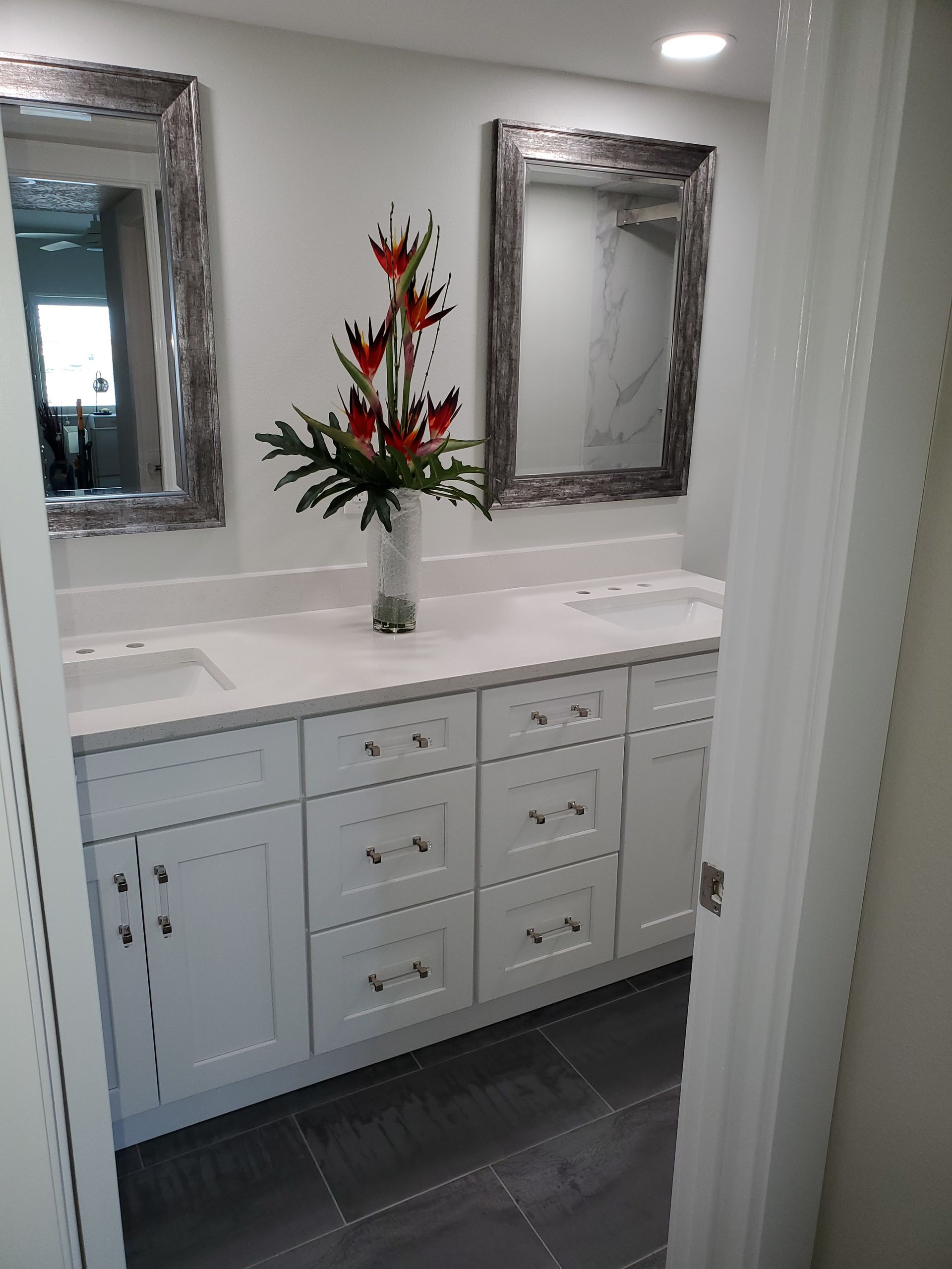 A double vanity bathroom with white cabinets, a white countertop, two framed mirrors, and a flower arrangement.