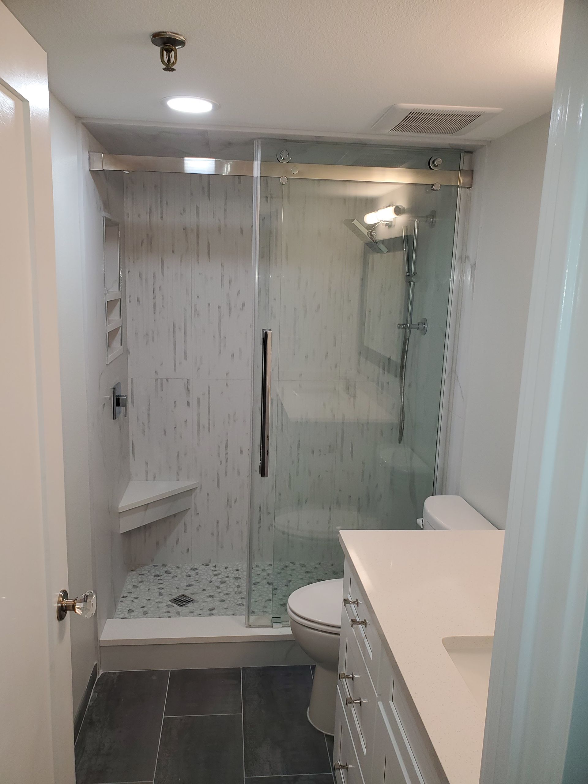 Modern bathroom featuring a tiled walk-in shower with a glass door, a floating white vanity, and dark floor tiles.
