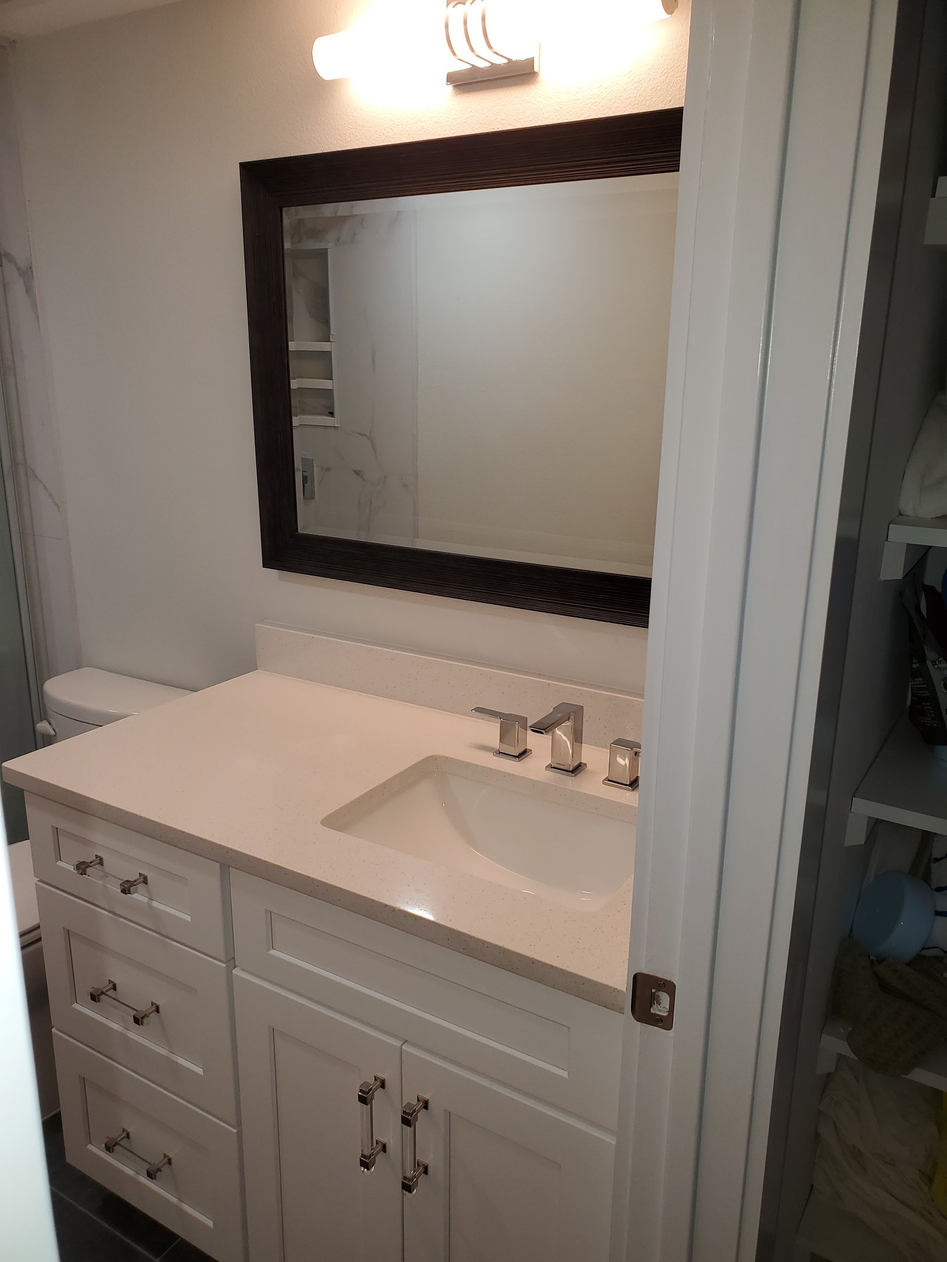 A bathroom vanity with a white countertop, sink, and faucet, featuring a dark-framed mirror and light grey cabinets.