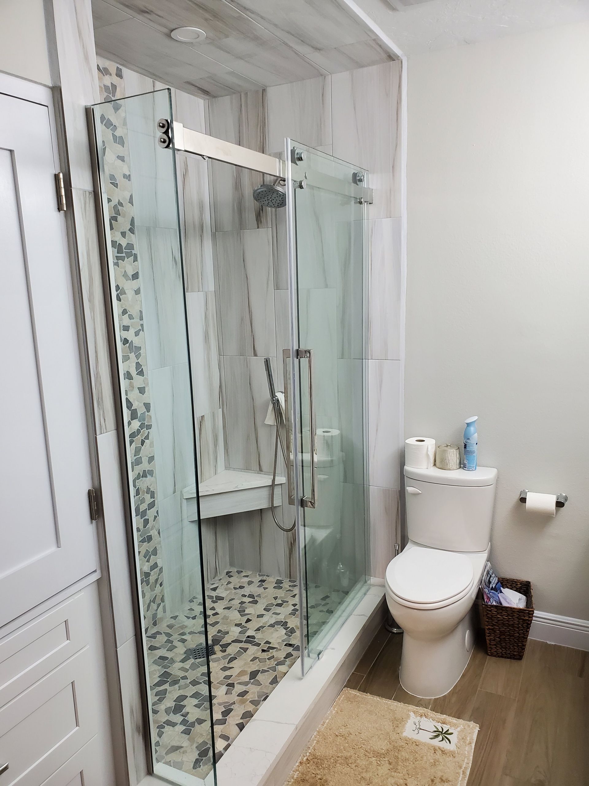 A bathroom with a tiled walk-in shower featuring a glass sliding door, next to a white toilet with a small wastebasket.