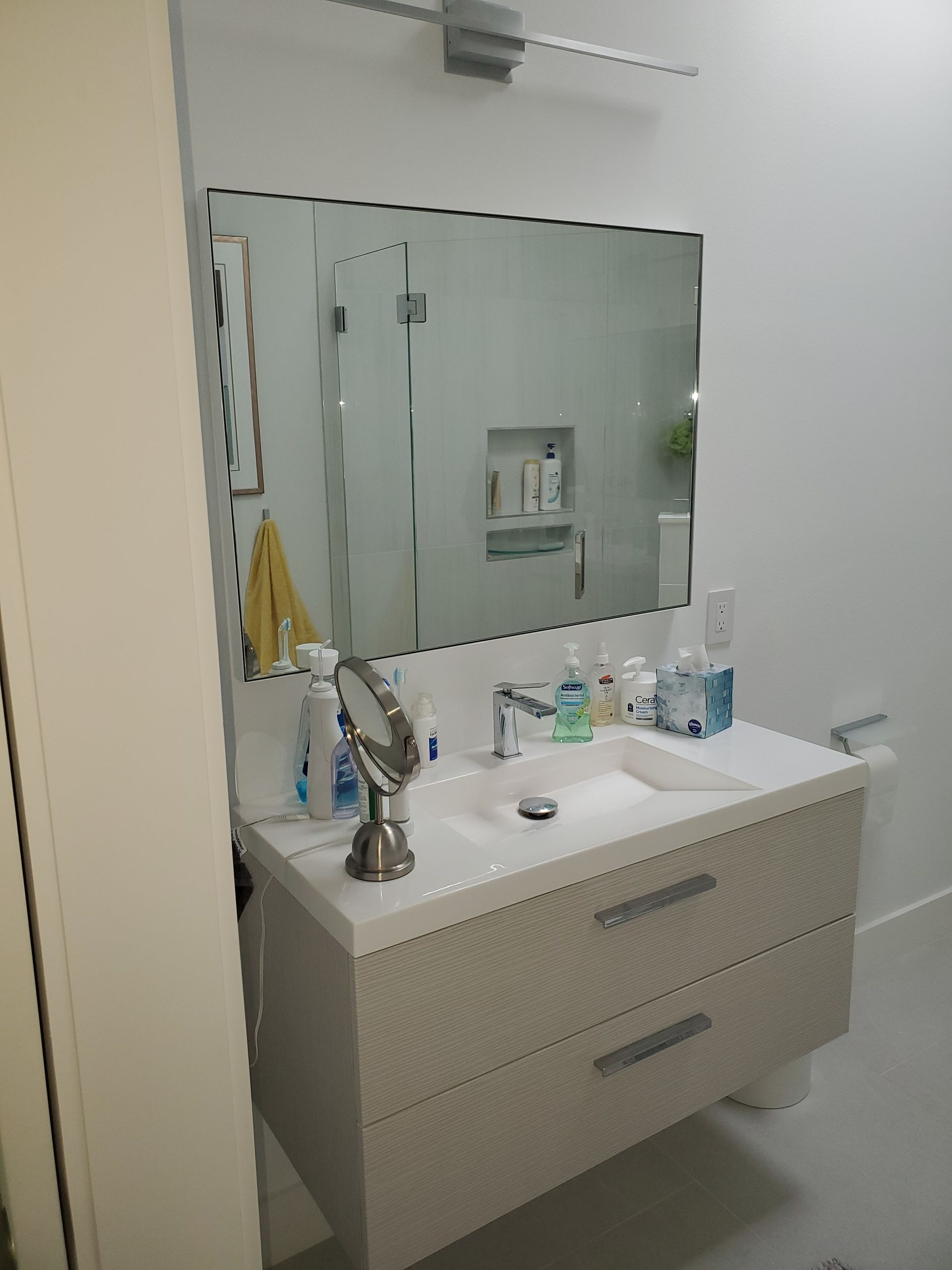 A wall-mounted bathroom vanity with a rectangular mirror, sink, and toiletries in a modern white bathroom.