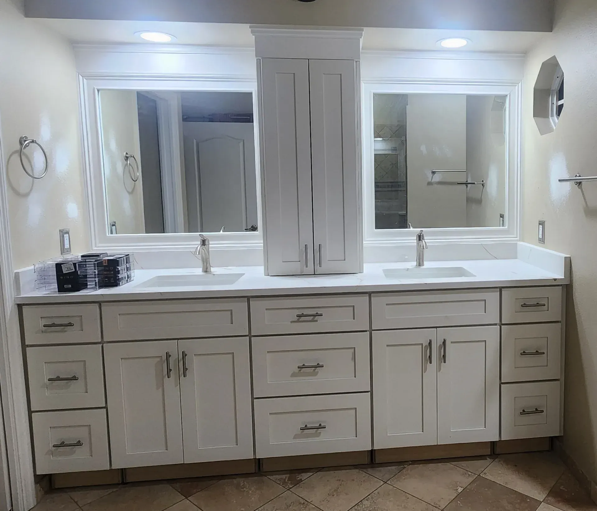 White bathroom vanity with two sinks, mirrors, and a central cabinet.