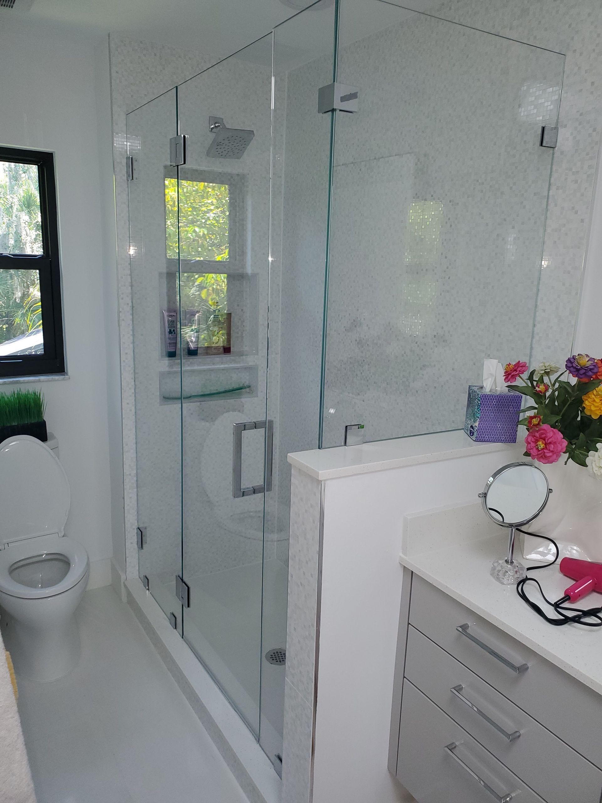 A modern bathroom featuring a white toilet, a walk-in glass shower, and a white vanity with drawers.