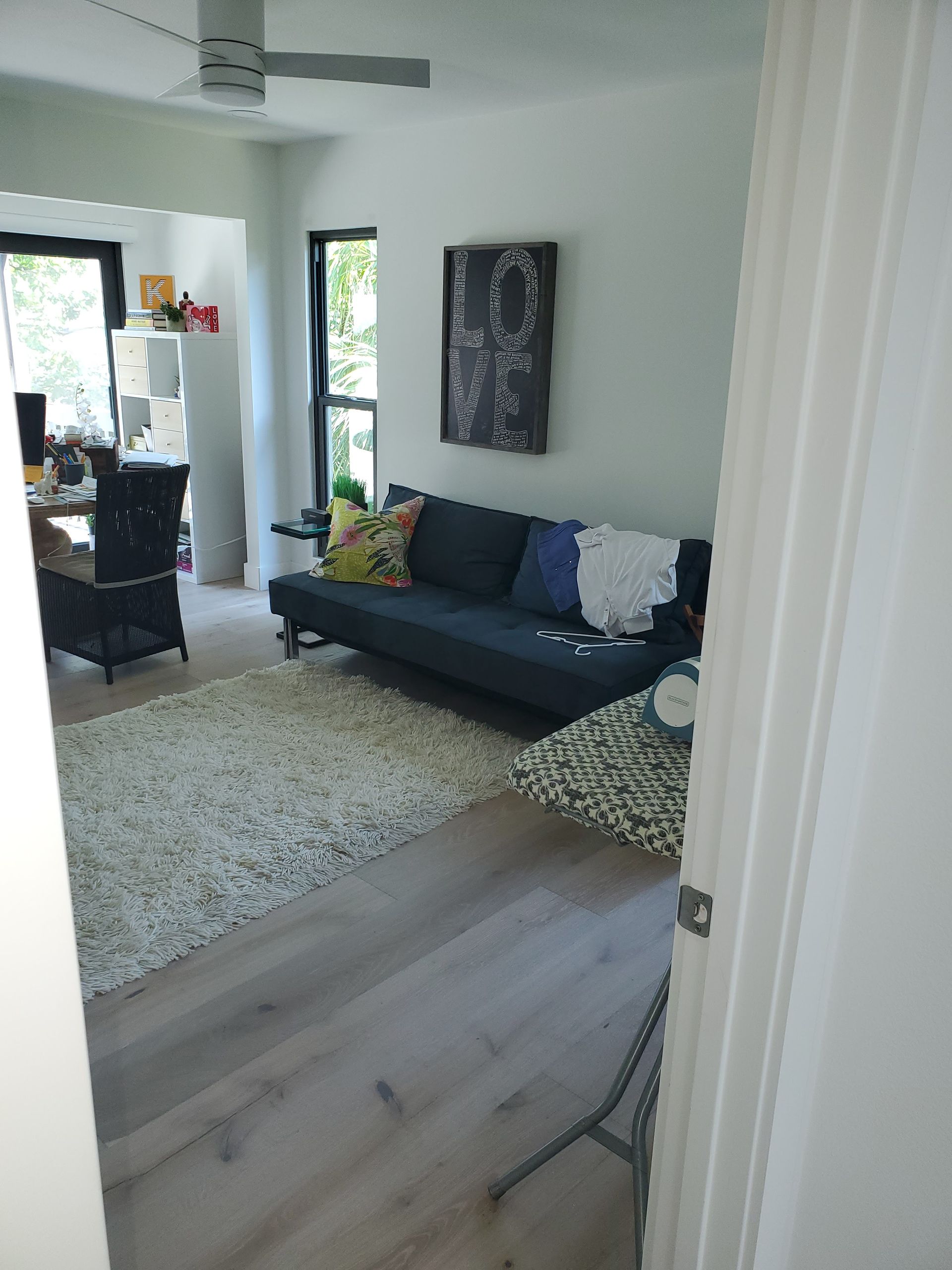 A living room with a dark blue sofa, a textured white rug, light wood flooring, and a dining area in the background.