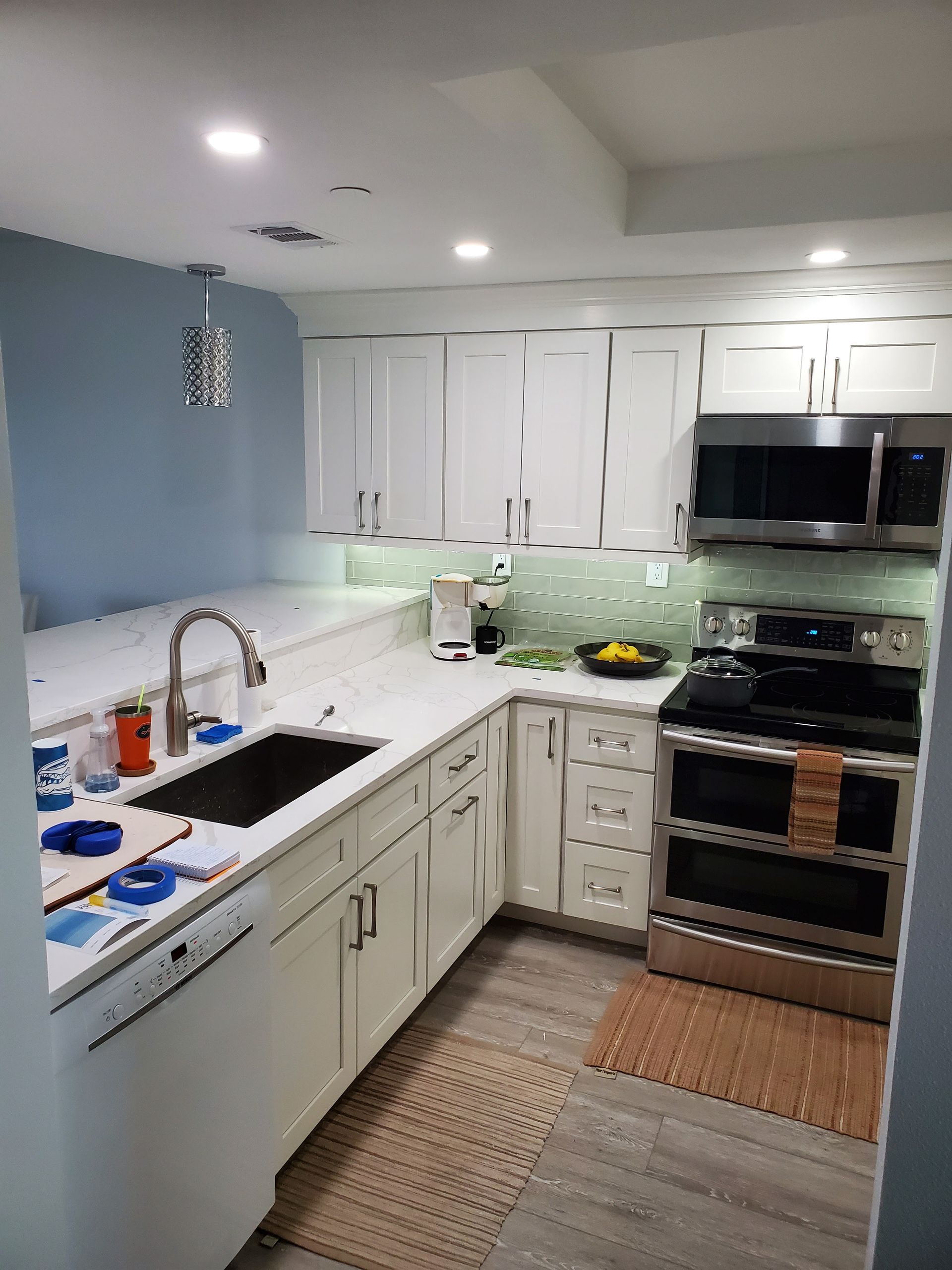 A bright kitchen with white cabinets, light countertops, a stainless steel stove, and a blue wall.