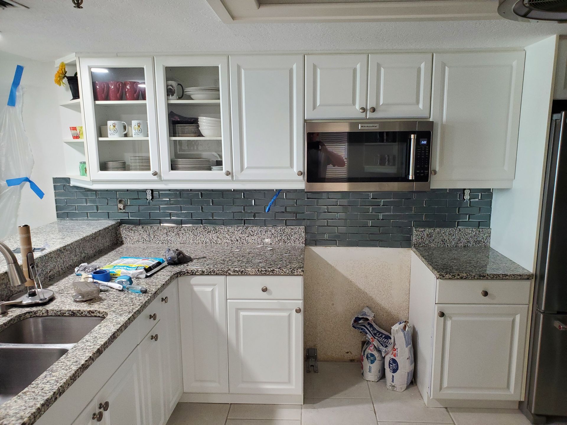 White kitchen cabinets with granite countertops and a dark gray tile backsplash in an under-construction kitchen.