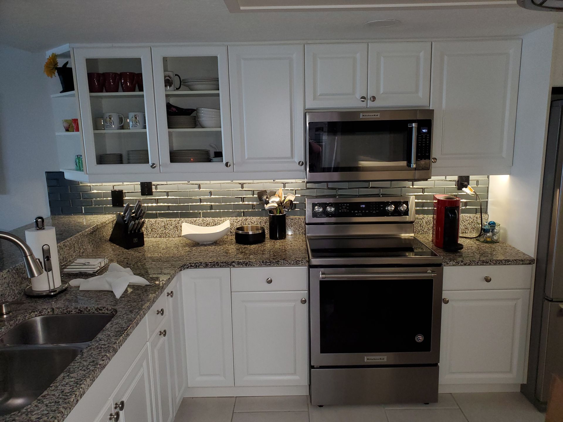 A kitchen with white cabinets, speckled granite countertops, stainless steel appliances, and a tiled backsplash.