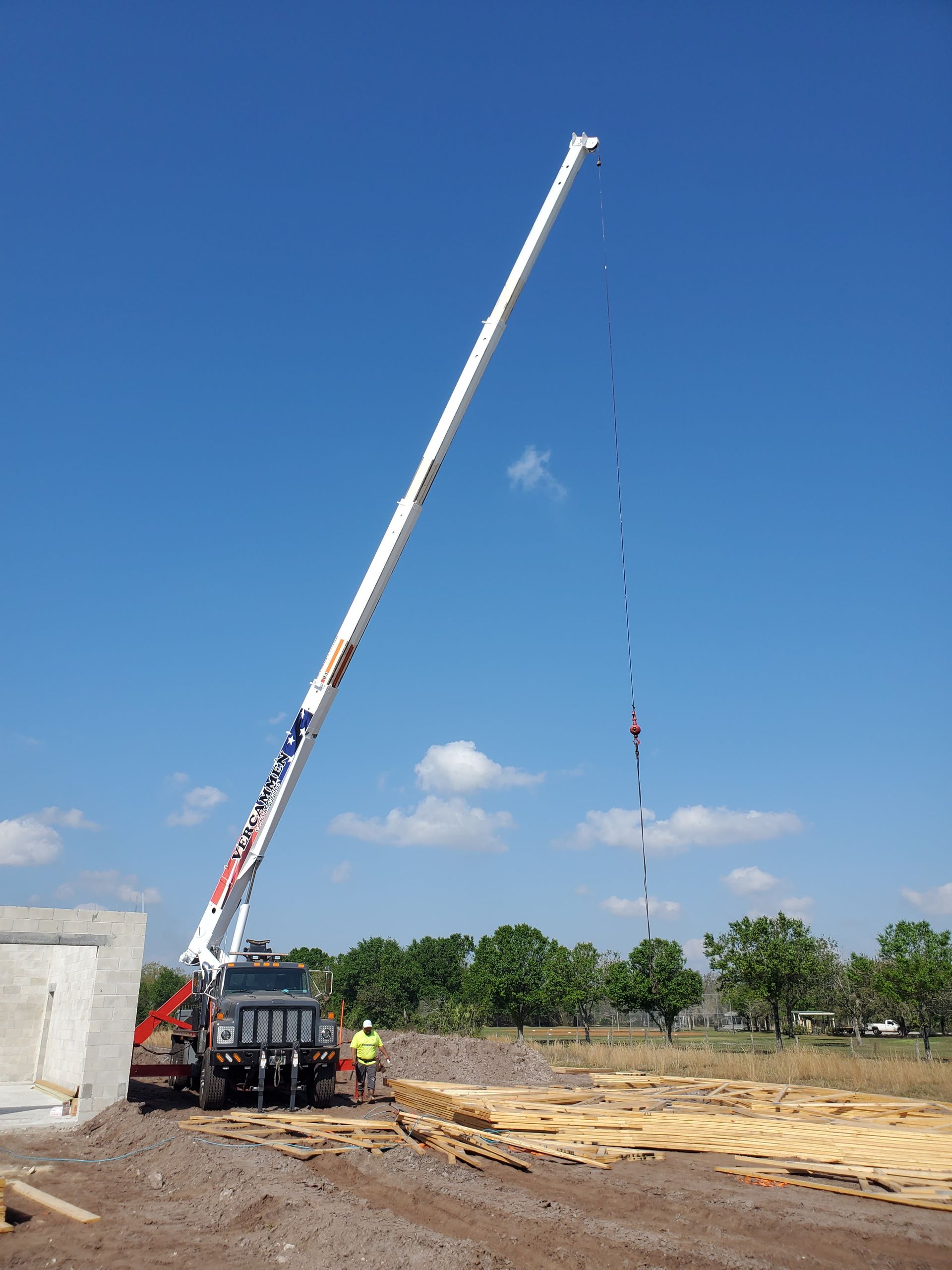 A crane with a long extended boom at a construction site against a clear blue sky.