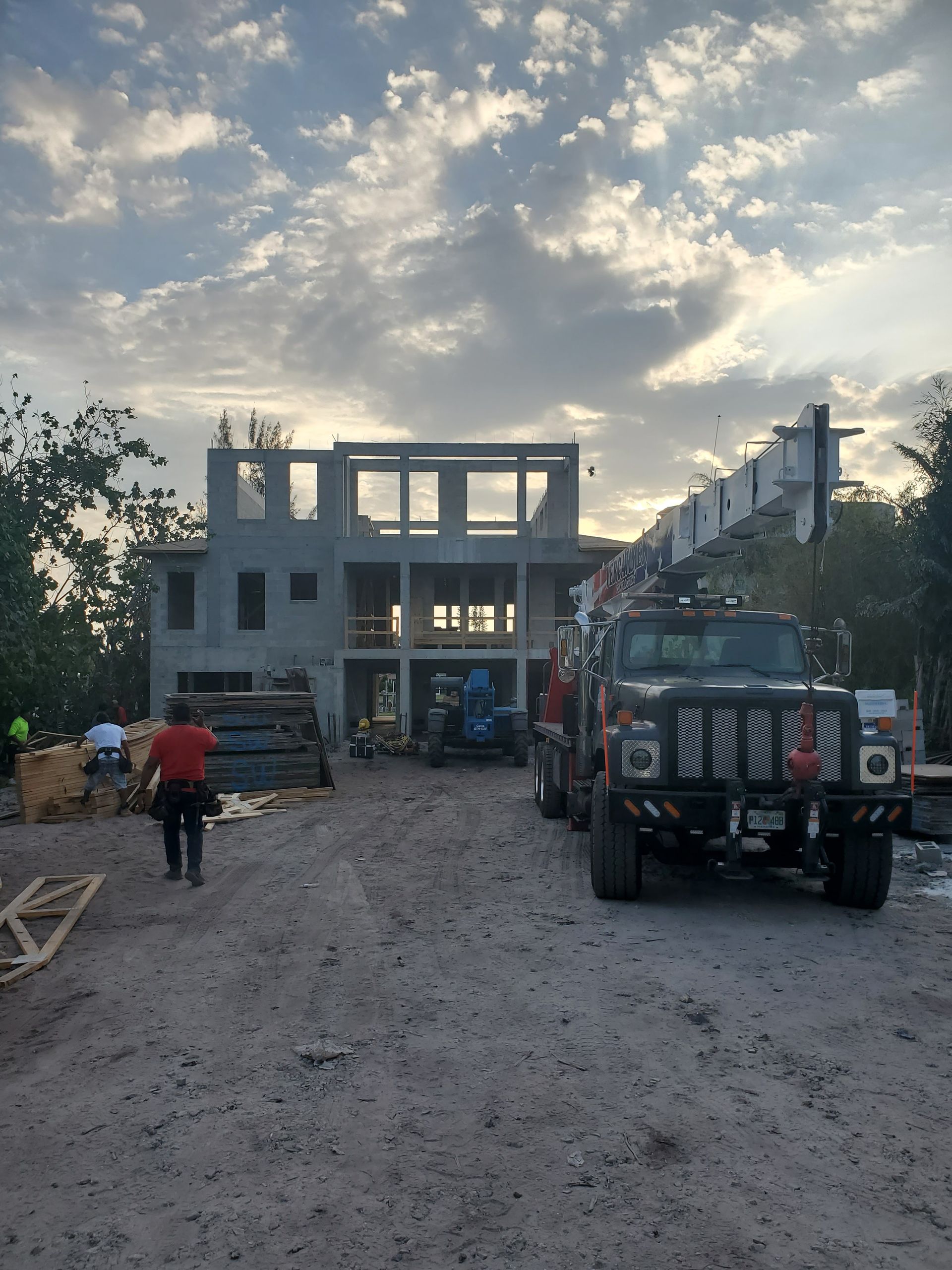 A crane truck parked at a construction site with an unfinished concrete multi-story building under a cloudy sky.