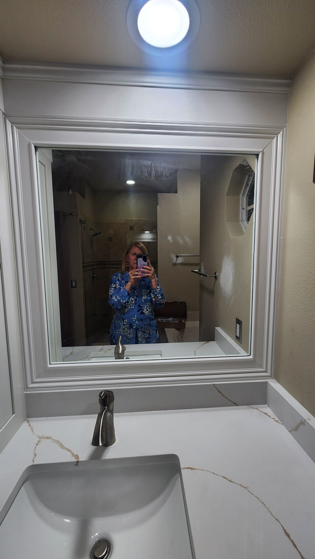 A bathroom mirror reflecting a person taking a photo in front of a white vanity with a single faucet.