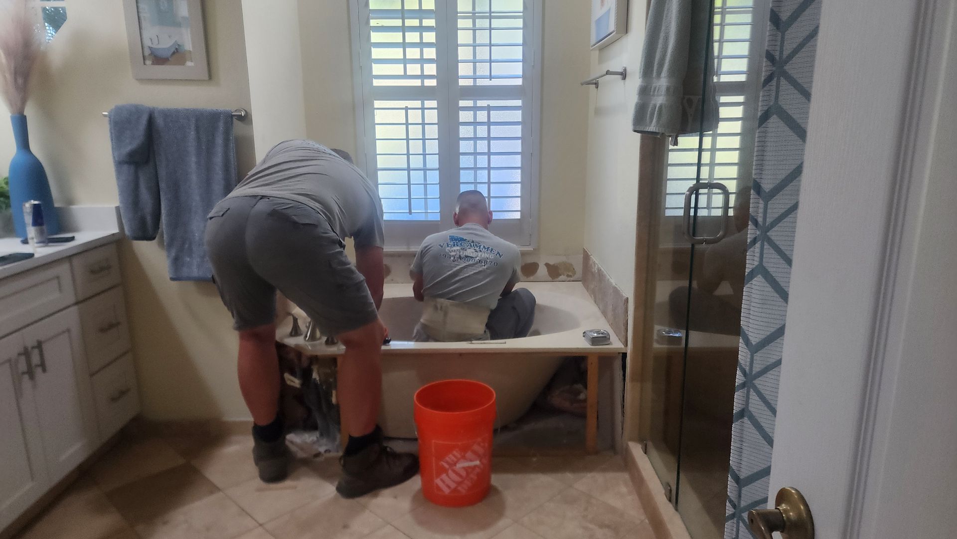 Two people work on installing a new bathtub in a bathroom, with one kneeling inside the tub and one standing outside.