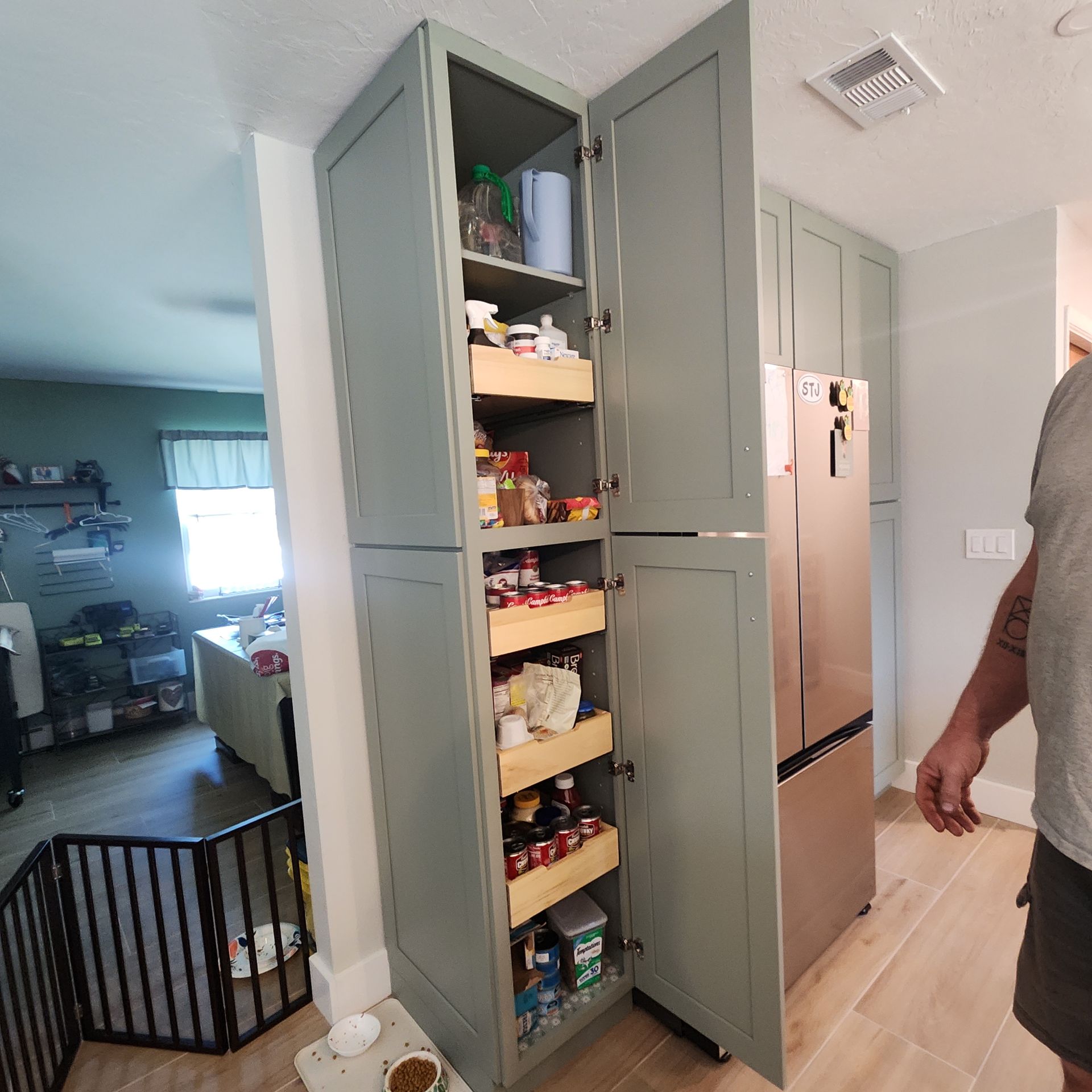 Tall, sage-green kitchen pantry cabinet with open doors revealing multiple wooden slide-out drawers full of items.