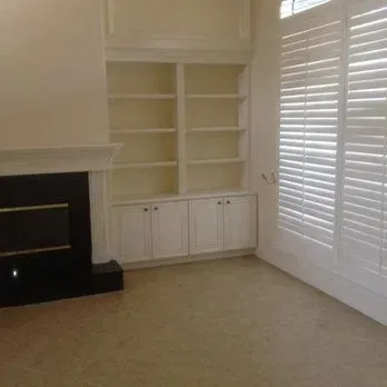 A living room with built-in bookshelves, fireplace, and window with shutters.