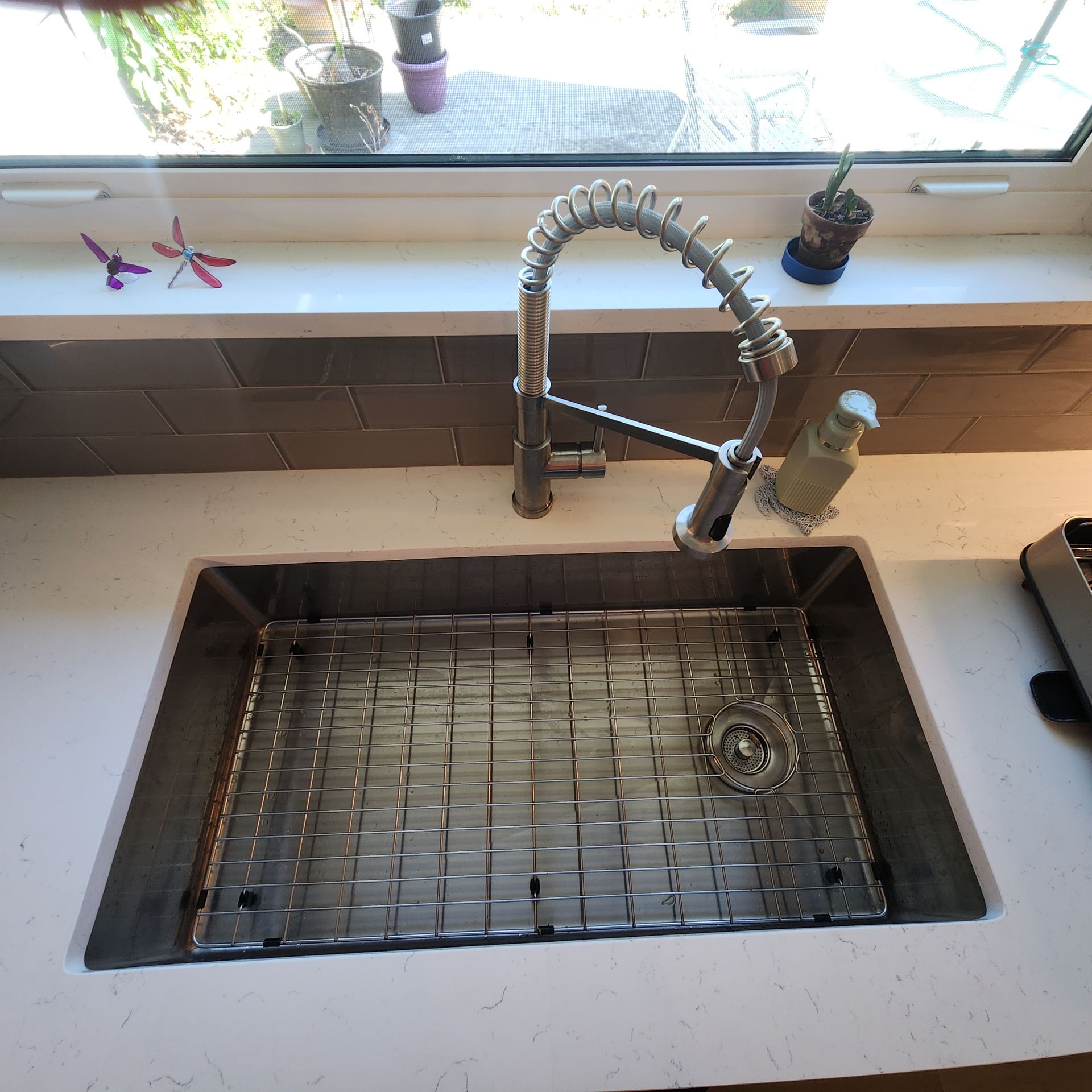A stainless steel kitchen sink with a spring-spout faucet and a wire grid basin rack on a white quartz countertop.