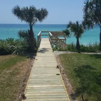 Wooden boardwalk leading to a beach overlook with palm trees and turquoise ocean view.