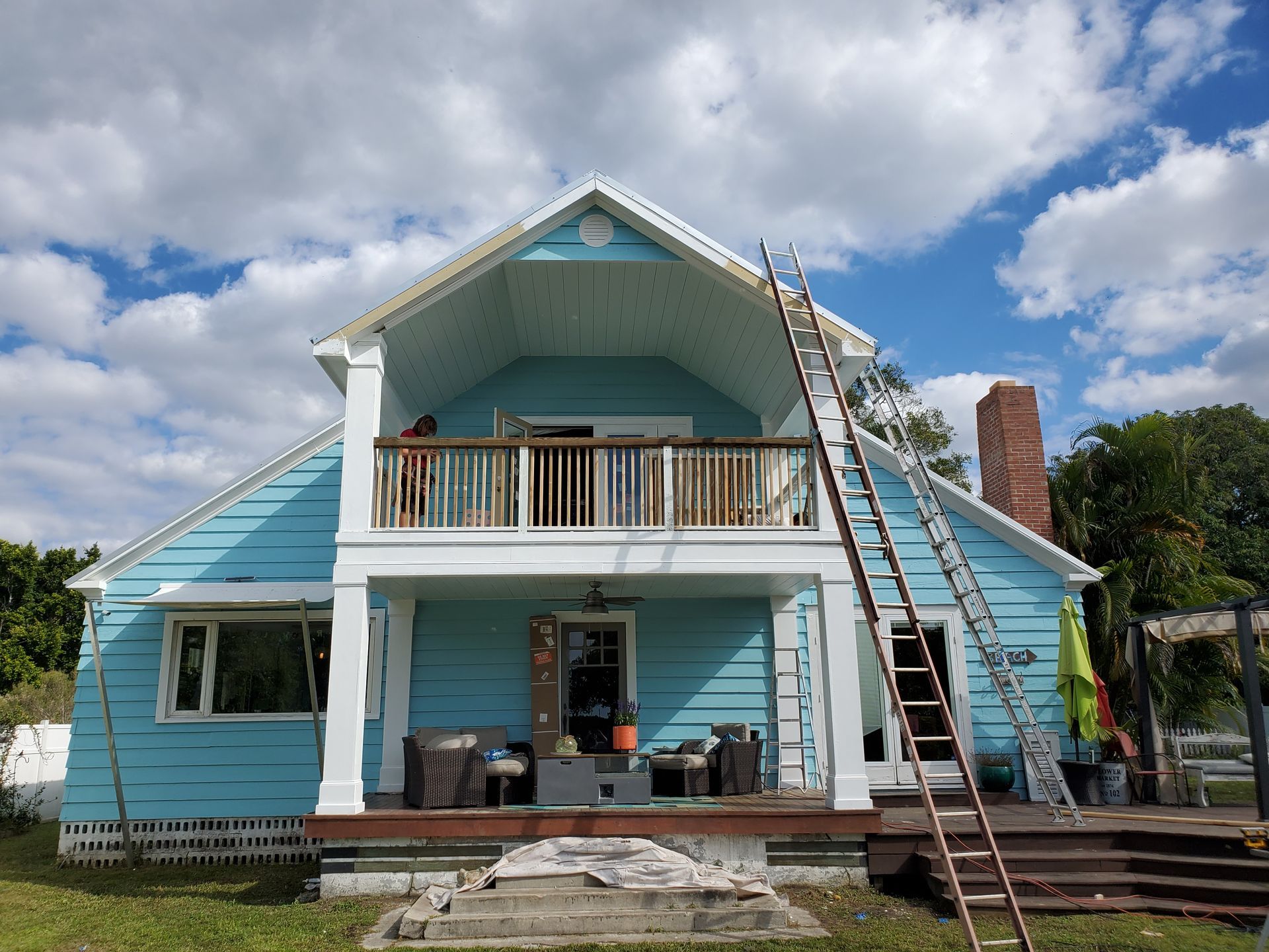 Light blue two-story house with a wooden balcony, white trim, and an extension ladder leaning against the side.