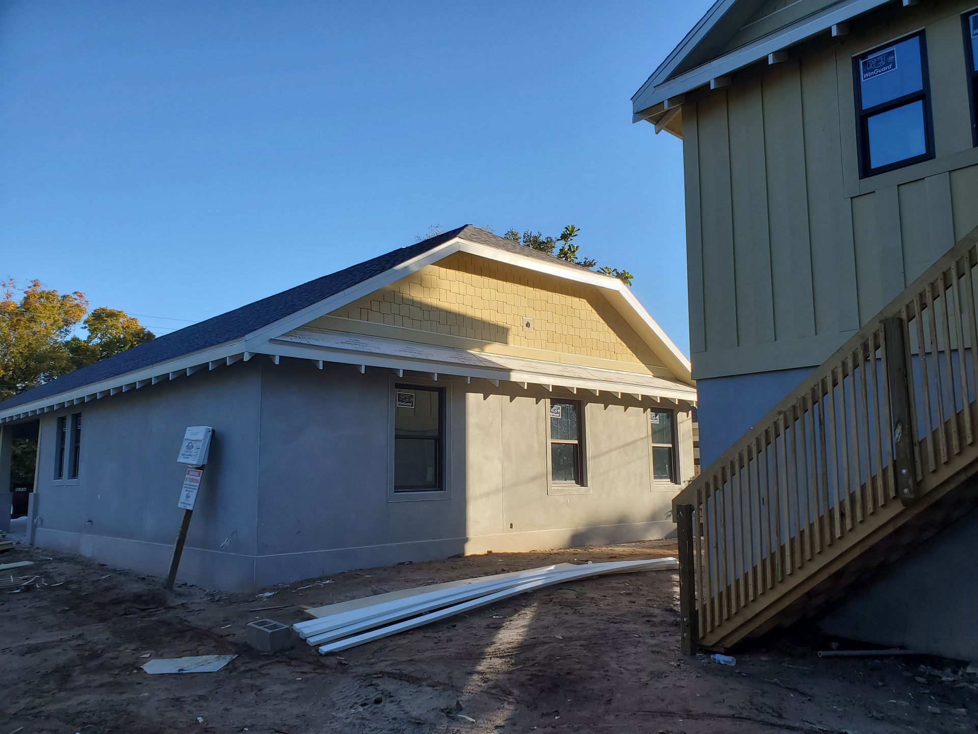A new construction site featuring a single-story gray house and a yellow two-story building with a wooden staircase.