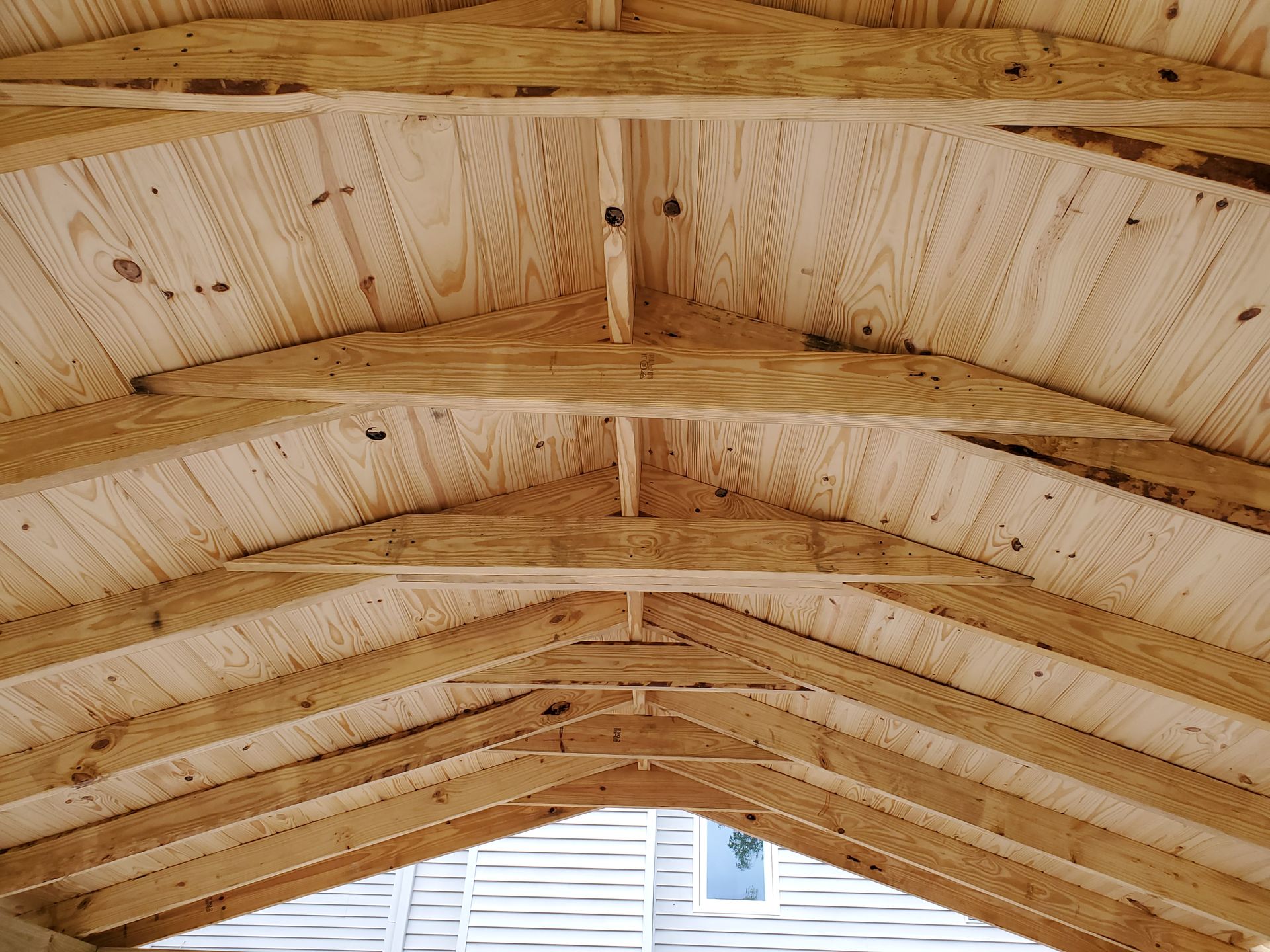 The underside of a wooden roof frame showing rafters, trusses, and plywood sheathing.