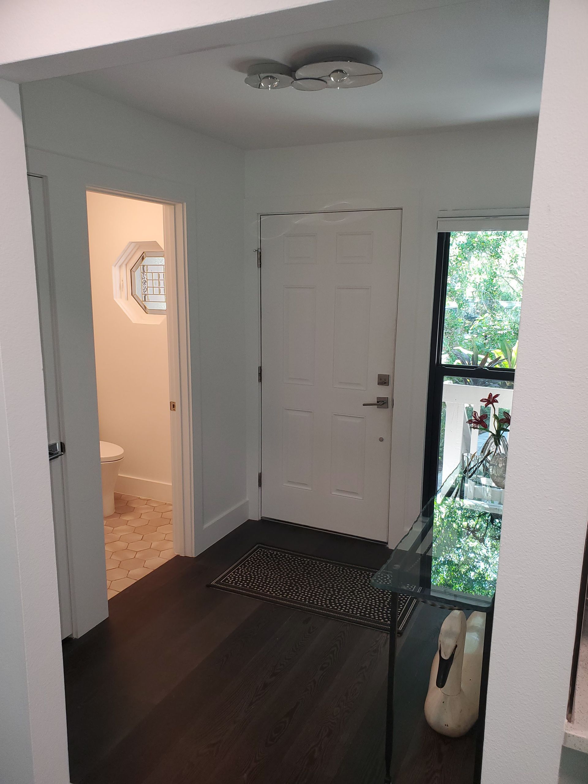 A hallway with dark wood floors leading to a white door, a patterned rug, and a glimpse into a bathroom.