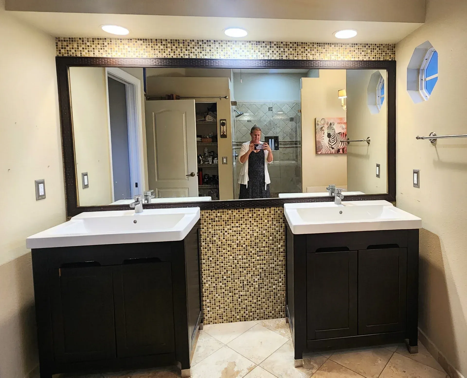 Bathroom with two dark vanities, large mirror, and person taking a photo in reflection.