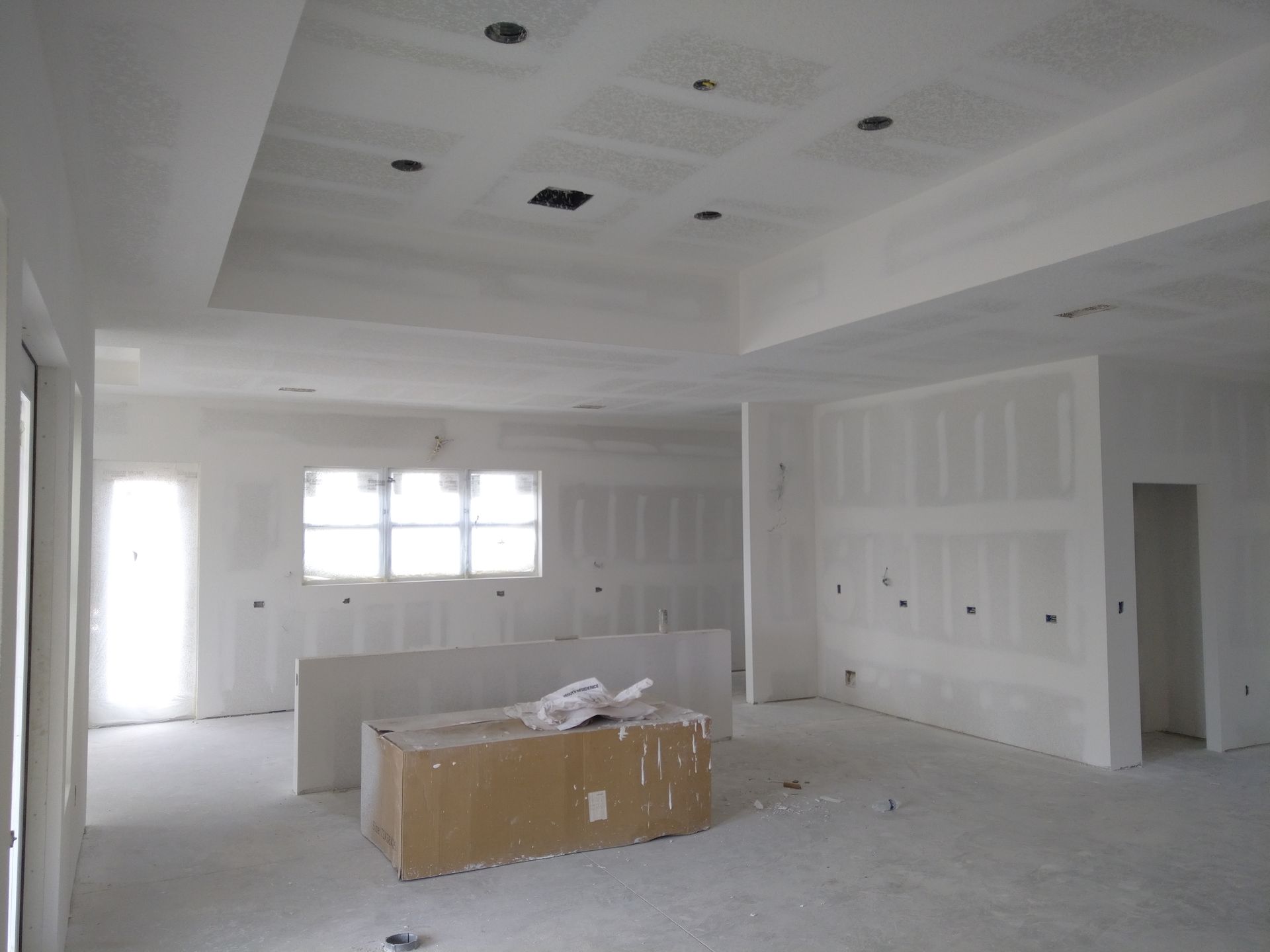 An interior view of a room under construction with white drywall, a recessed ceiling, and a box on the floor.