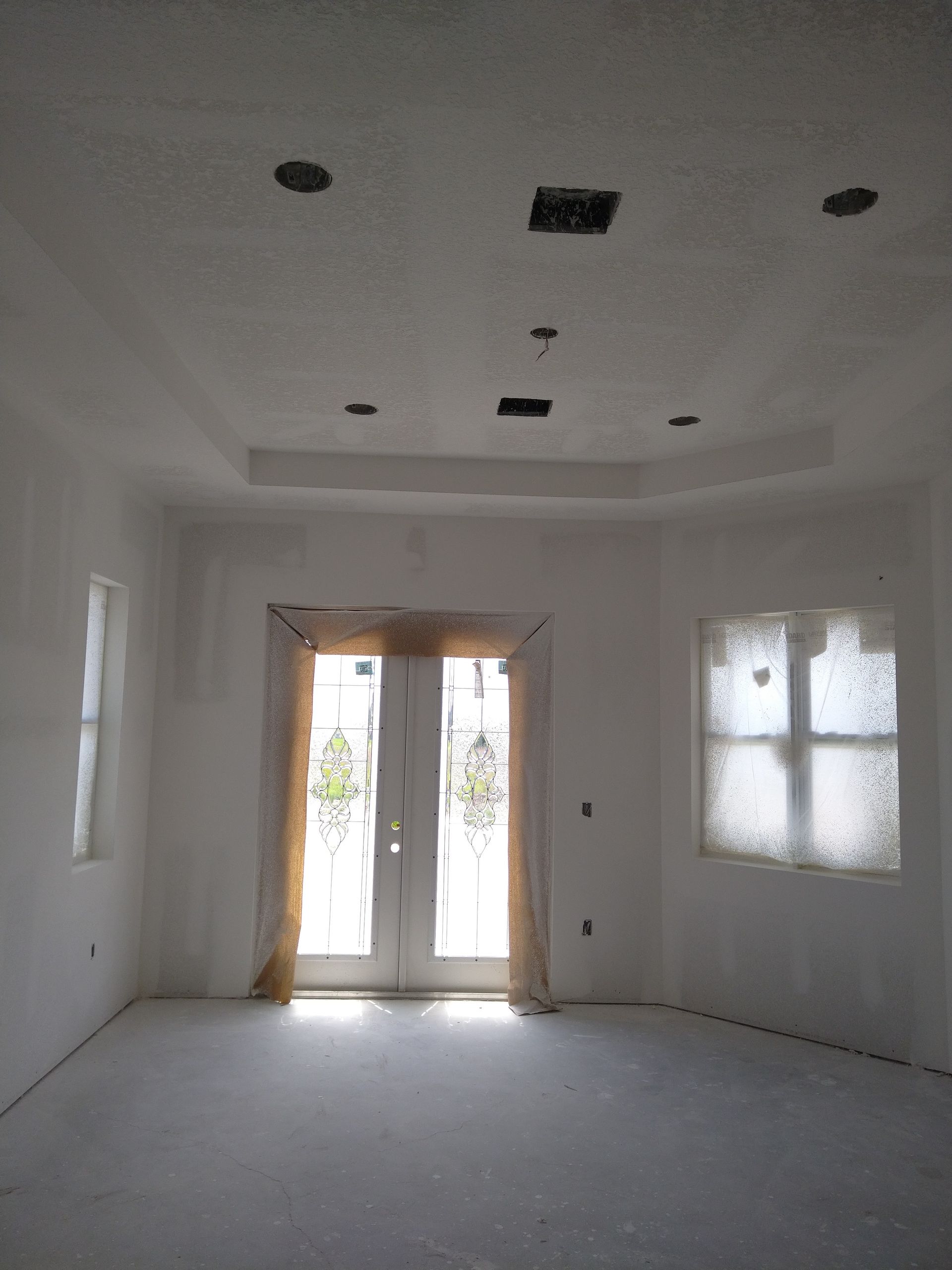 An unfinished interior room with bare drywall, a tray ceiling with recessed lighting holes, and a front entryway door.