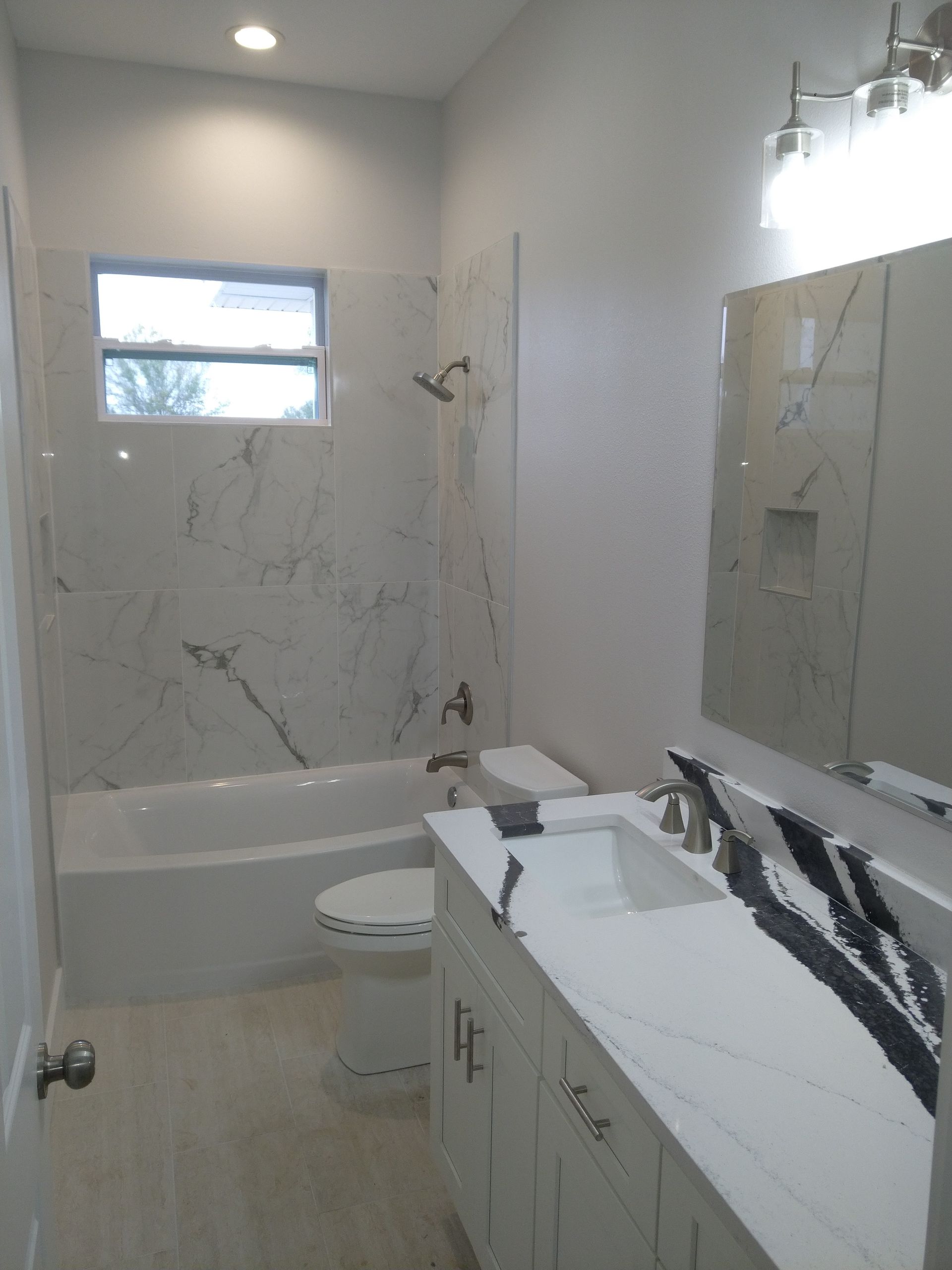 A modern bathroom featuring a white vanity with black-veined marble countertop, a toilet, and a marble-tiled tub shower.