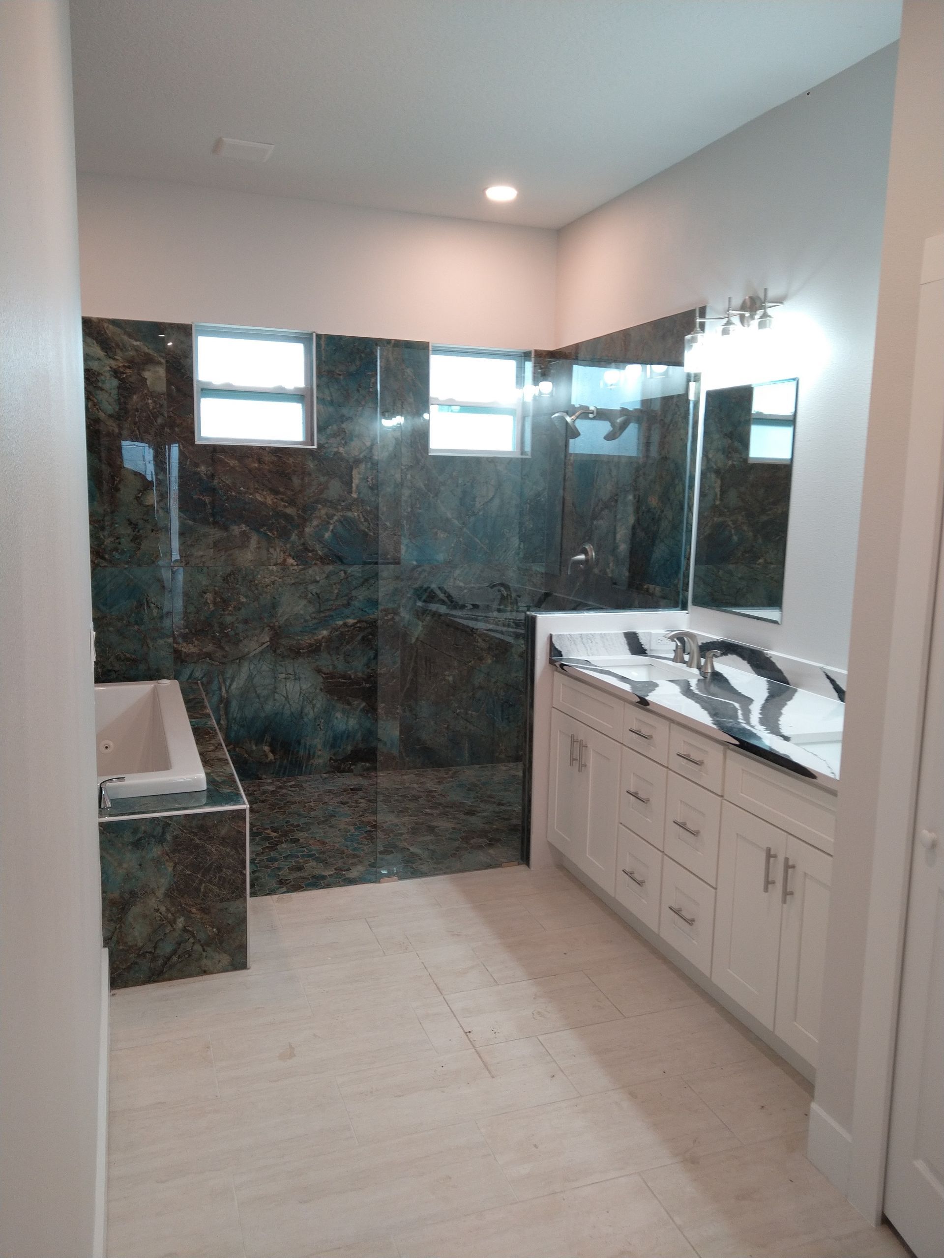 Modern bathroom with a white vanity, a marbled countertop, and a shower area with dark stone wall tiles.