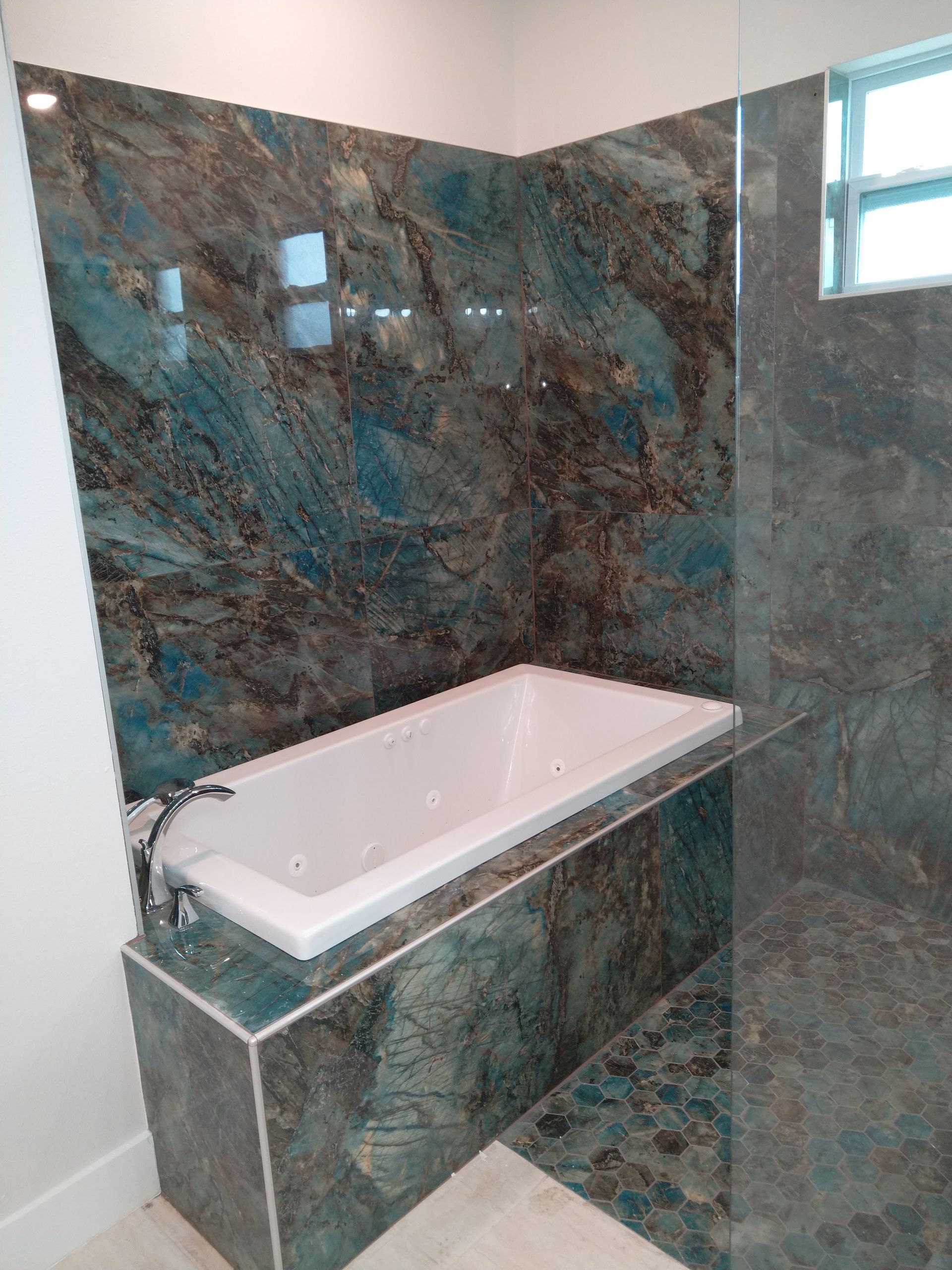A white soaking tub set against a wall and front panel covered in striking, multi-toned blue and brown marbled stone.