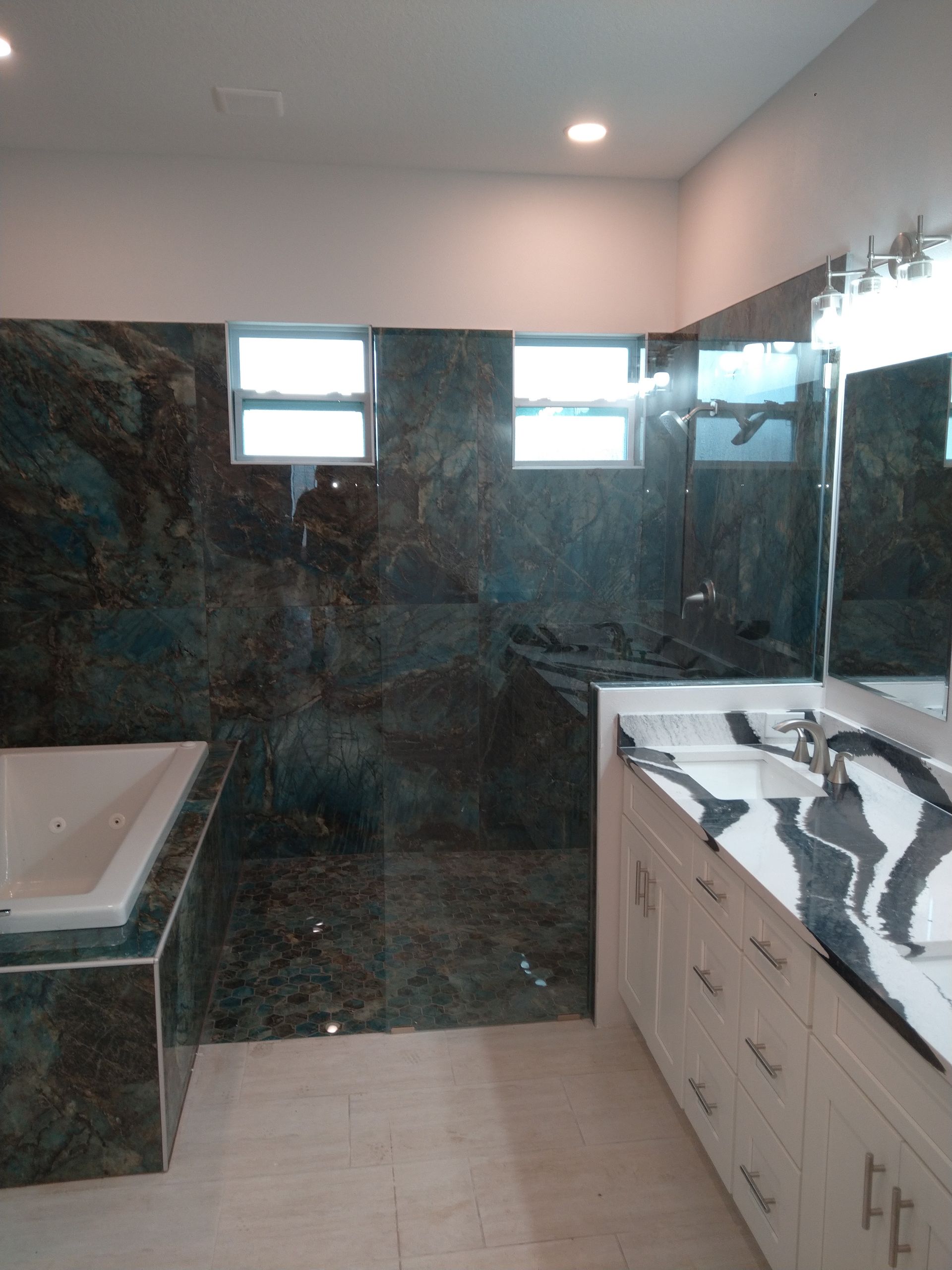 A modern bathroom featuring a white vanity with black-veined marble countertops, a bathtub, and a glass-enclosed shower.