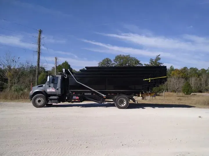 Black dump truck on a dirt road, raised bed, against a blue sky, trees in the background.