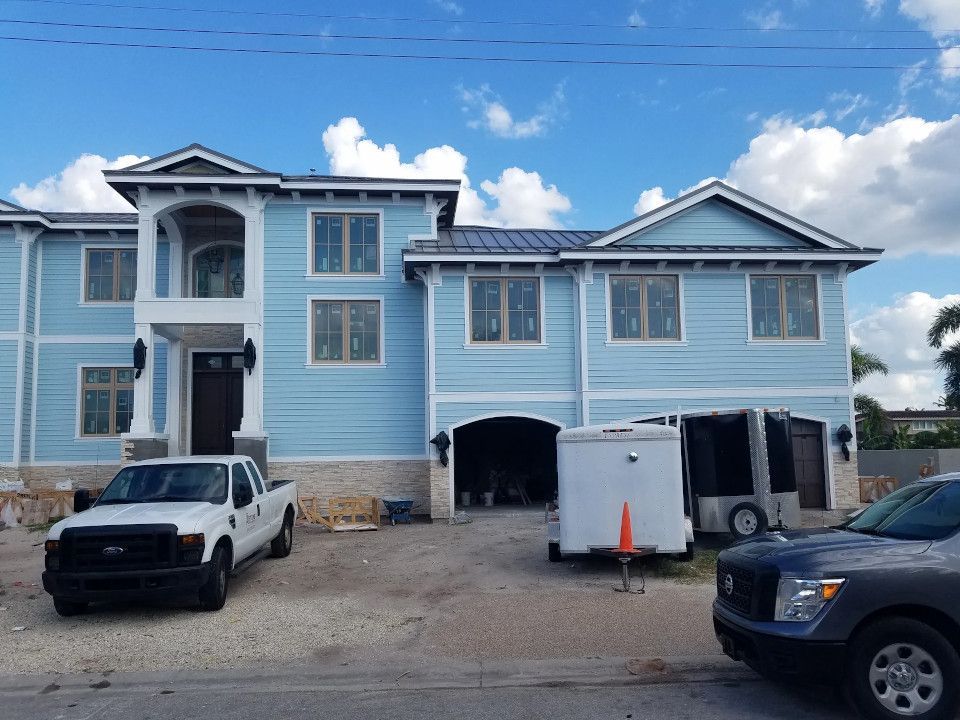 Light blue two-story house under construction with a white truck and trailer parked in front on a gravel driveway.