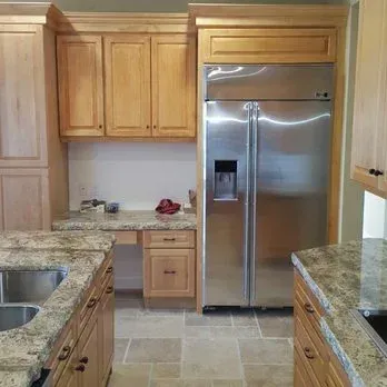 Kitchen with granite countertops, wooden cabinets, stainless steel refrigerator, and stone tile floor.