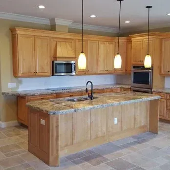 Kitchen with light wood cabinets, granite countertops, island with sink, and pendant lights.