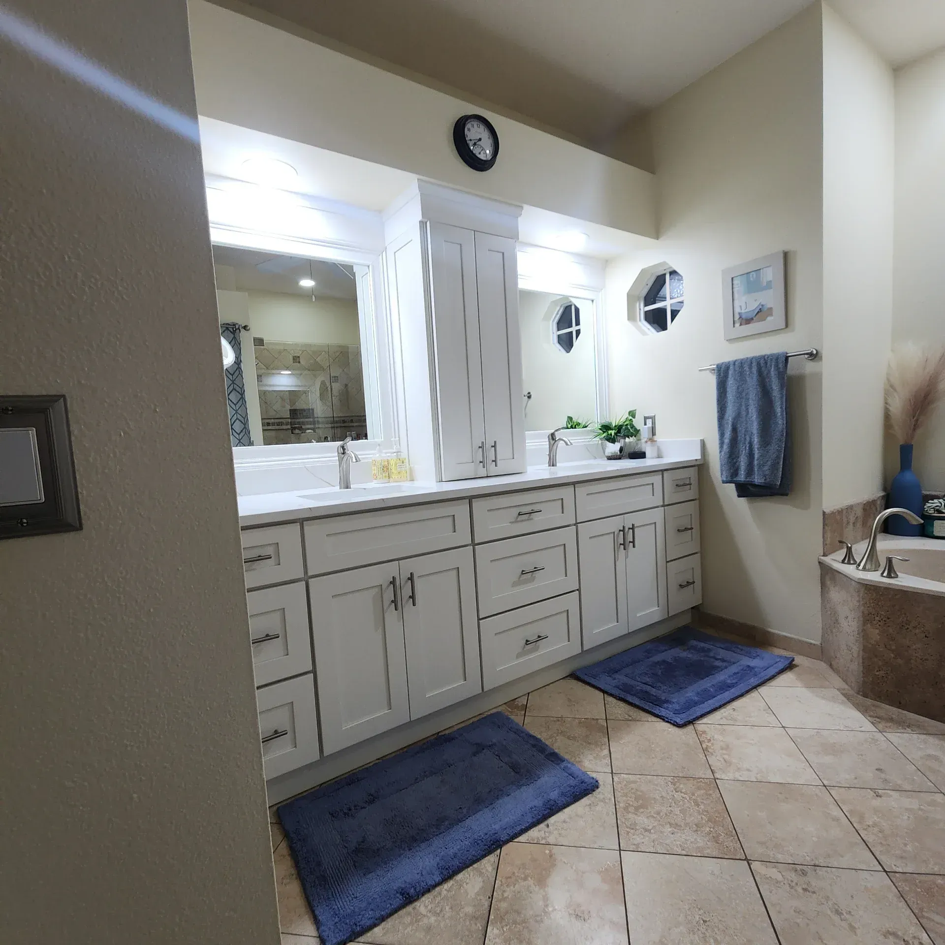 A white dual-sink bathroom vanity with tile flooring and two blue rugs in front of each sink area.