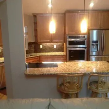 Kitchen with light-colored cabinets, granite countertops, and two pendant lights above a breakfast bar with two wooden stools.