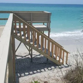 Wooden stairs and platform leading to a sandy beach and turquoise ocean.