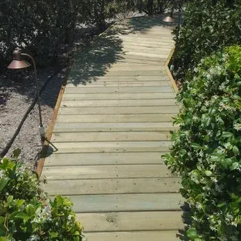 Wooden boardwalk pathway through greenery, with lights, leading into the distance.