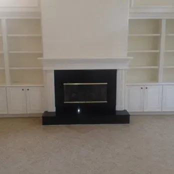 Fireplace with black surround, flanked by white bookshelves and cabinets.