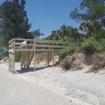 Wooden viewing platform with stairs on a sandy beach, surrounded by vegetation.