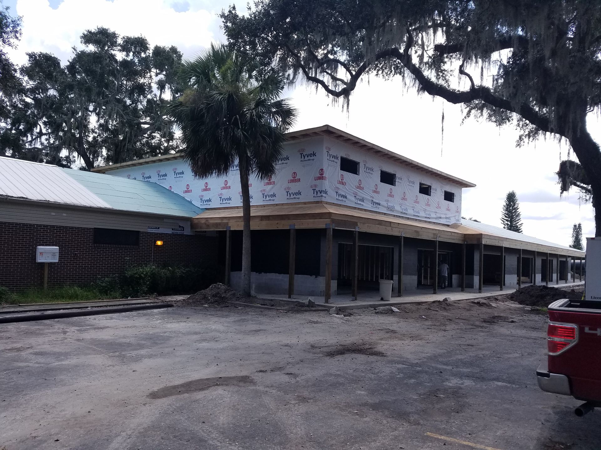 A single-story commercial building under construction with exposed framing and blue weather barriers, viewed from a lot.