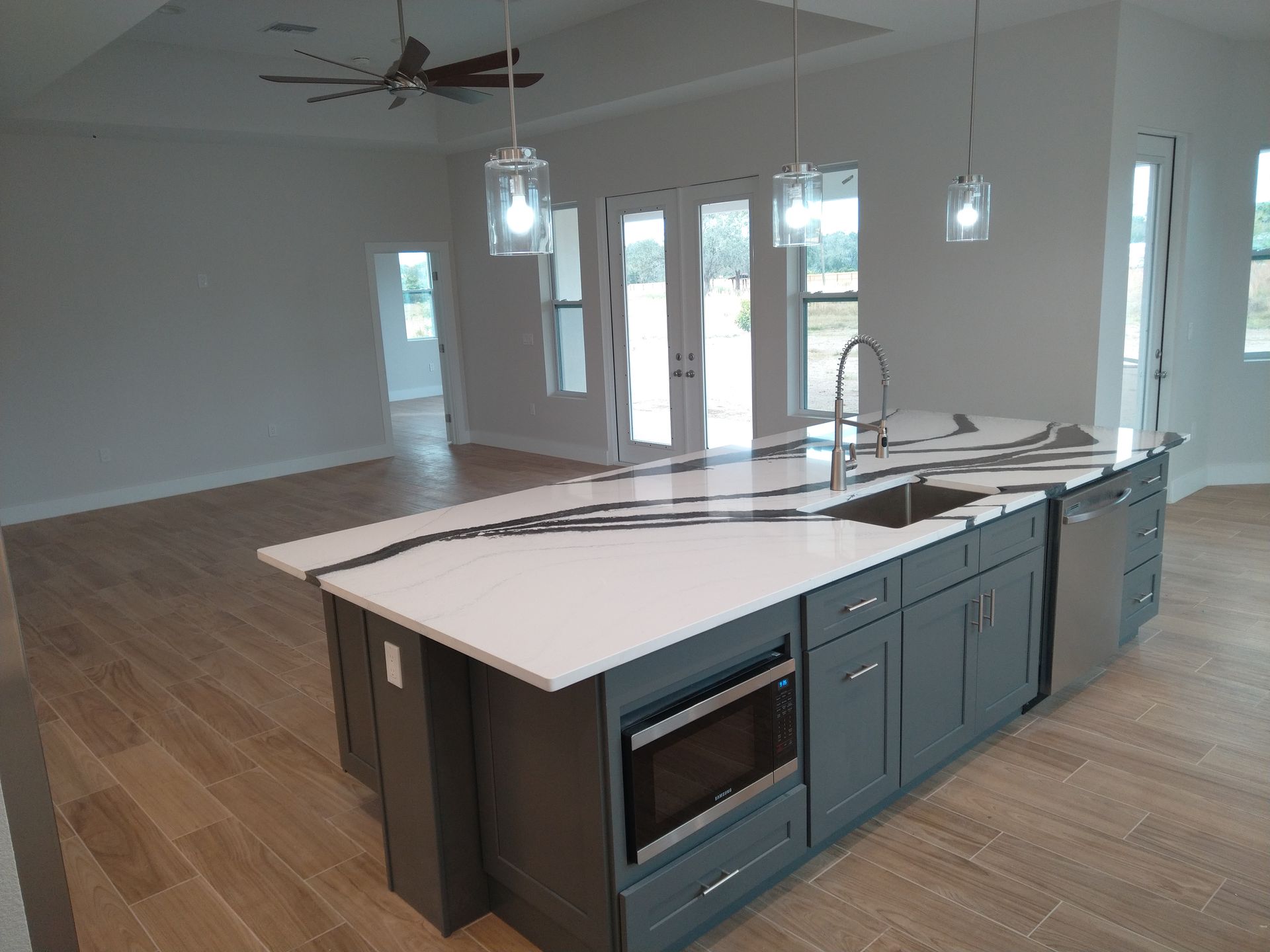 Modern kitchen island with dark gray cabinets, white marble countertop with black veining, and three glass pendant lights.