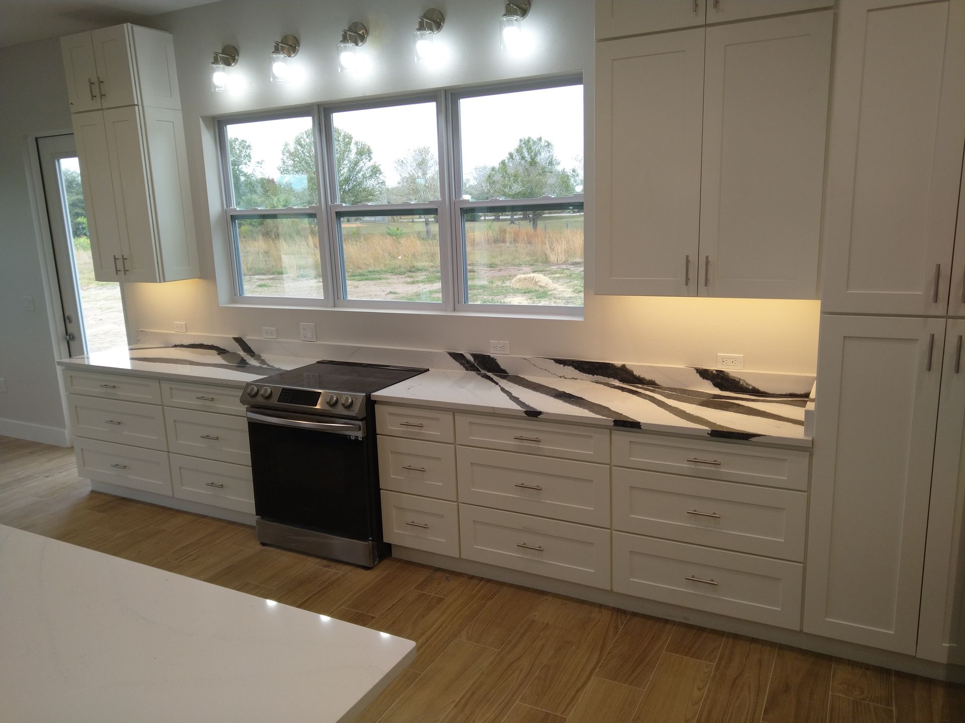 A modern kitchen featuring white cabinets, a black stove, light wood floors, and quartz countertops with dark veining.