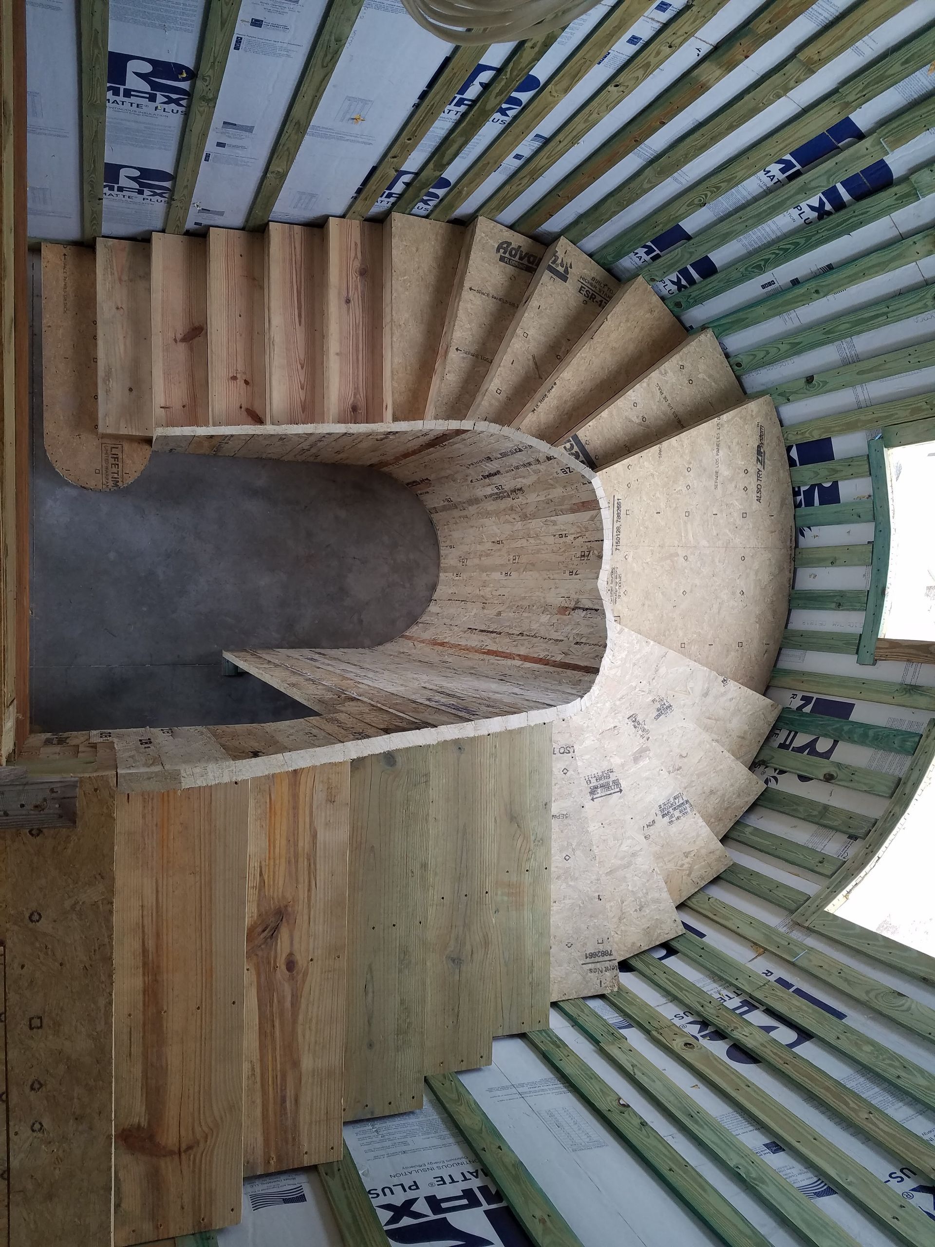 A curved staircase made of plywood and lumber under construction in a wood-framed room with insulated walls.