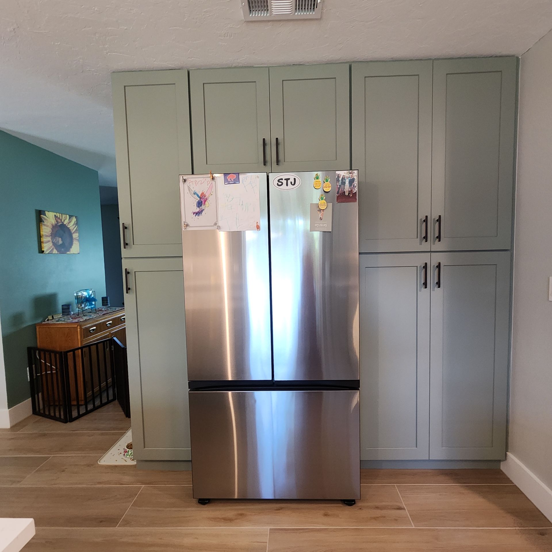 Stainless steel refrigerator built into sage green cabinetry in a kitchen with light wood flooring.