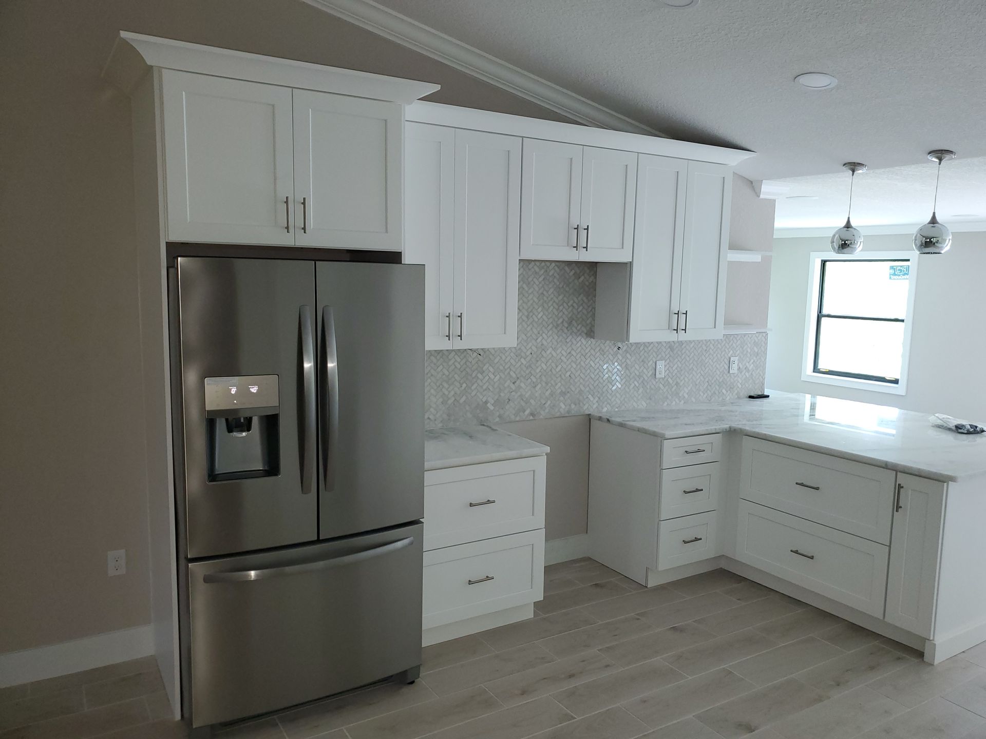 A modern kitchen featuring white shaker cabinets, a stainless steel refrigerator, and a light-colored countertop.